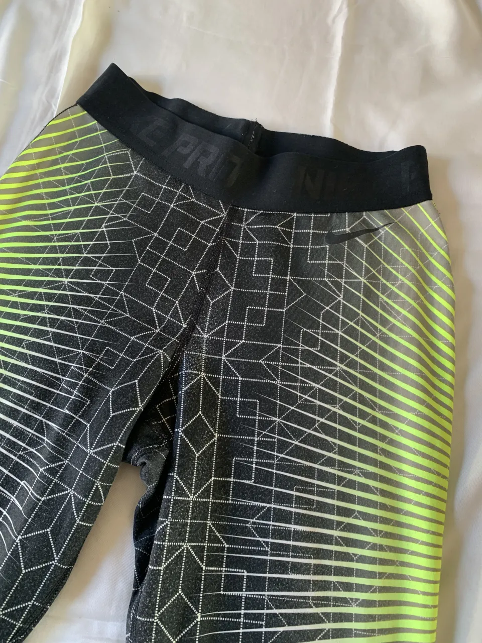 Calzas deportivas Nike Pro con estampa geométrica en degradé de verde flúo a negro. Ideales para entrenar y sentirte cómoda.