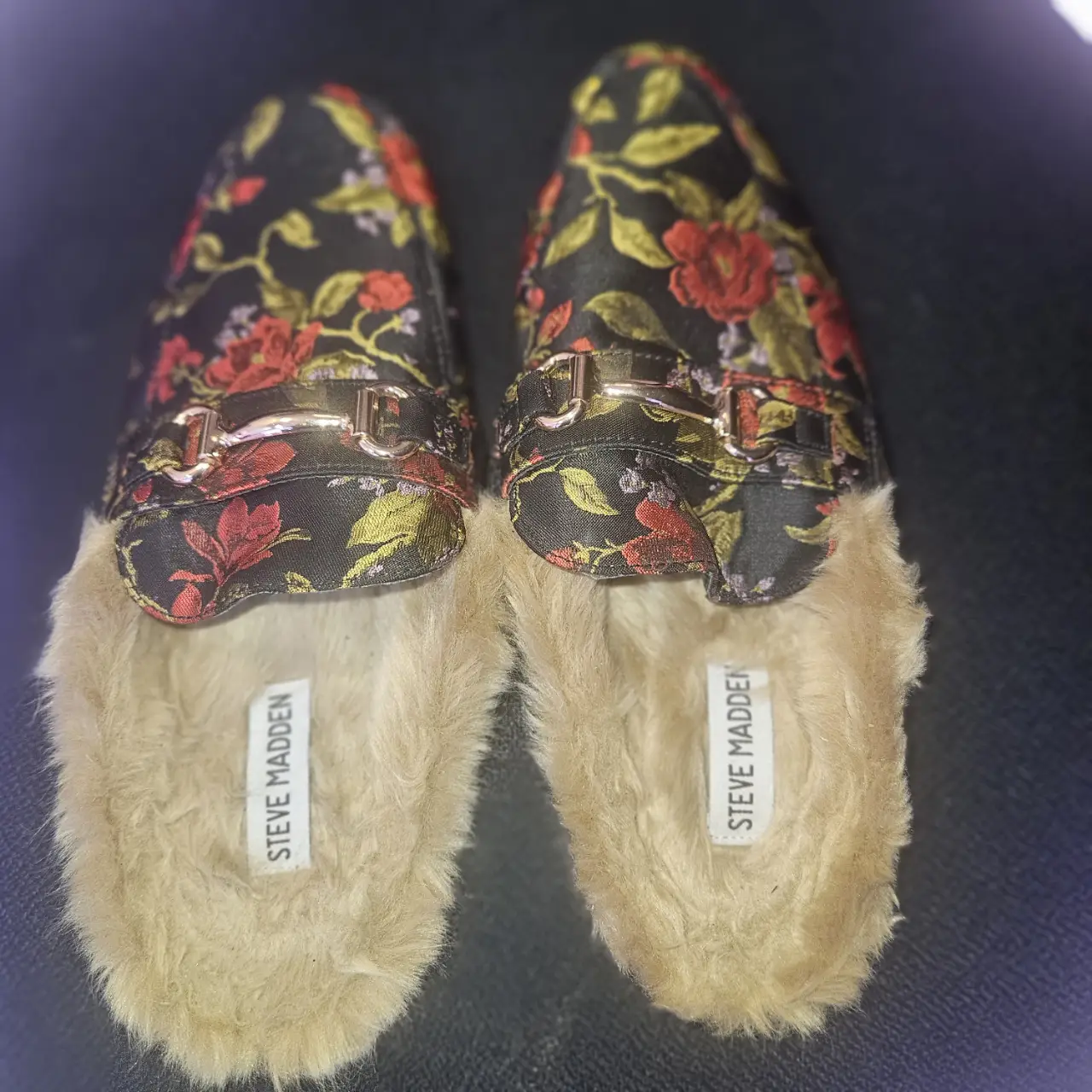 Zuecos de mujer con estampado floral en tonos rojos y verdes sobre fondo negro. Interior de piel sintética color beige. Detalles dorados en la hebilla. Marca Steve Madden.