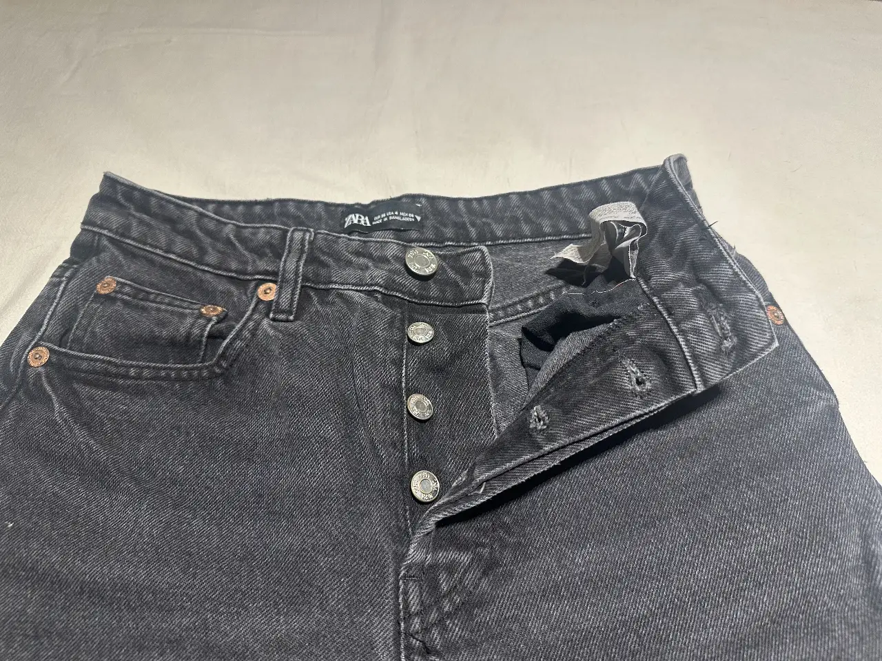 Jeans rectos negros de Zara, talle 26. Tiro medio, con botones y bolsillos clásicos. Perfecto para un look casual y versátil.