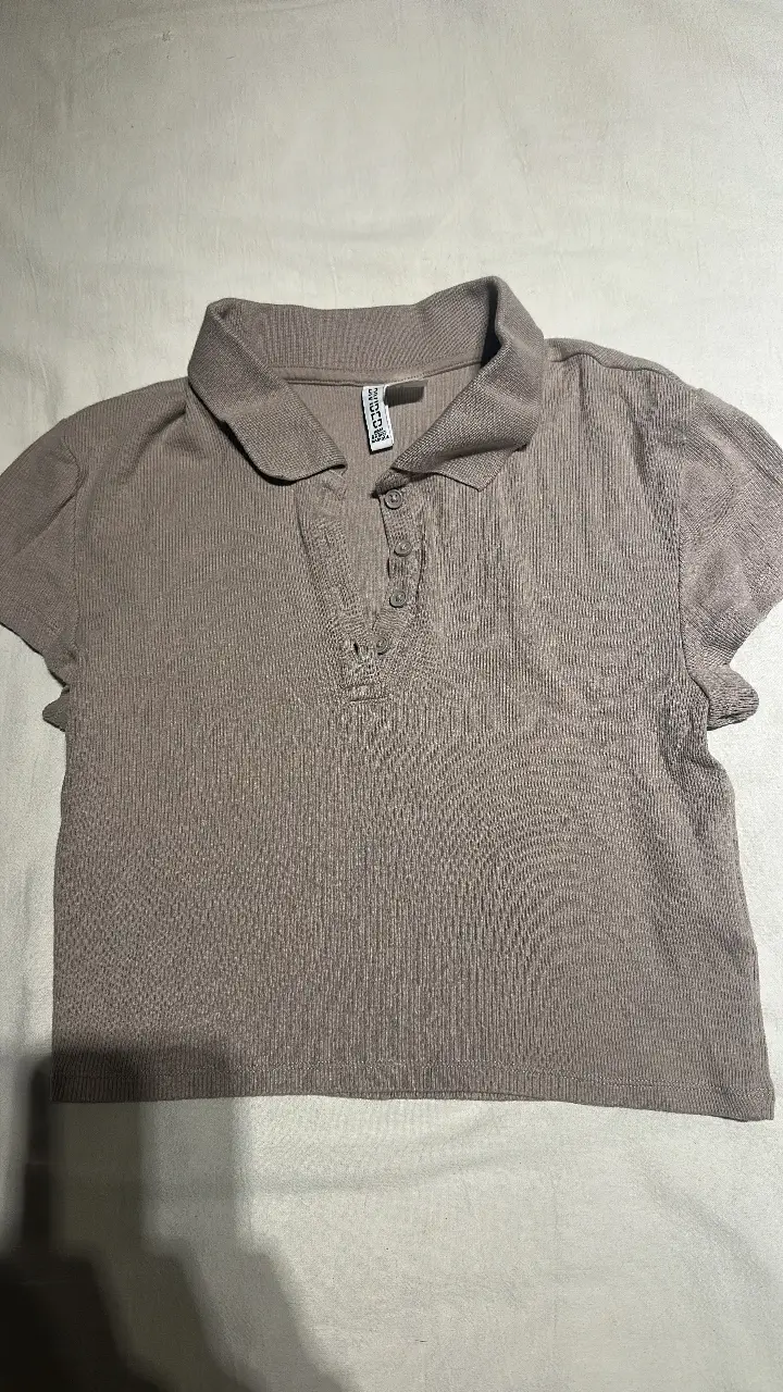 Remera tipo polo de tejido acanalado en color beige. Cuello camisero y tres botones en la parte delantera. Ideal para un look casual y moderno.