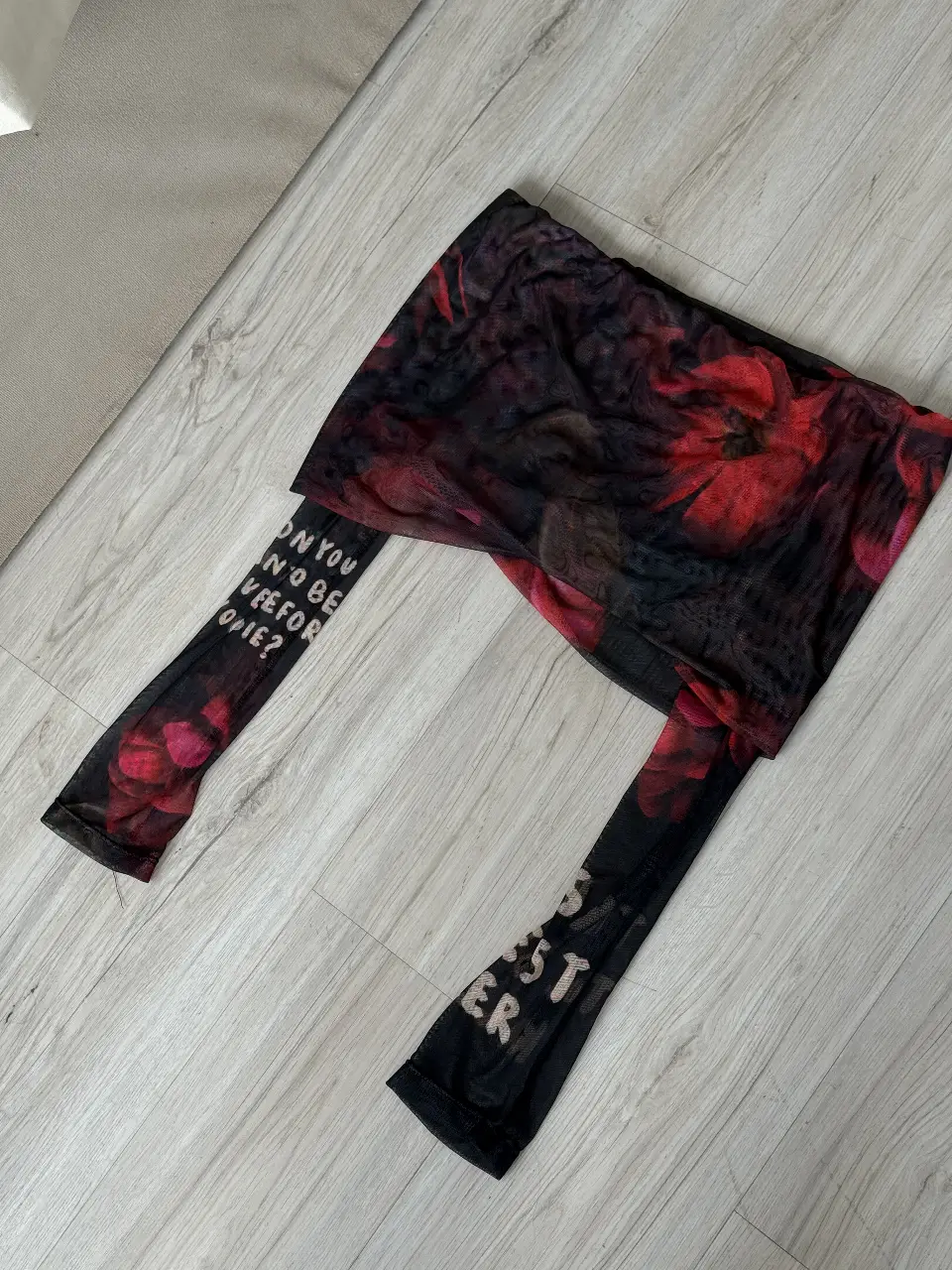 Top de red con estampado floral en tonos rojos y negros. Mangas largas con frase estampada en blanco. Ideal para un look audaz y moderno.