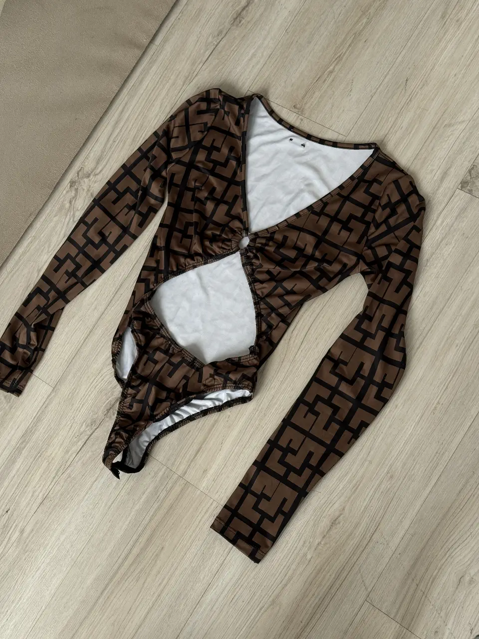 Body de manga larga con diseño geométrico en marrón y blanco. Corte en la cintura y escote pronunciado. Ideal para un look moderno y audaz.