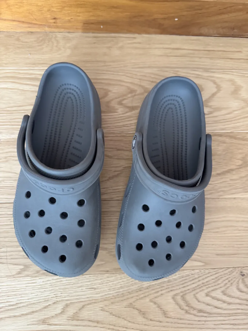 Ojotas Crocs grises de goma con tiras y orificios característicos de la marca.