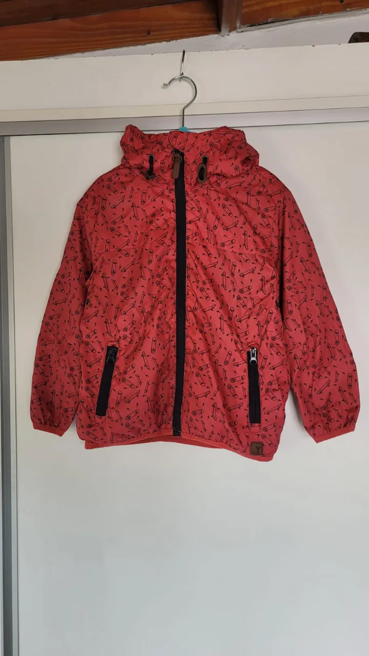 Campera roja con estampa de skateboards y rayos en negro. Tiene capucha, cierre al frente y bolsillos con cierre.