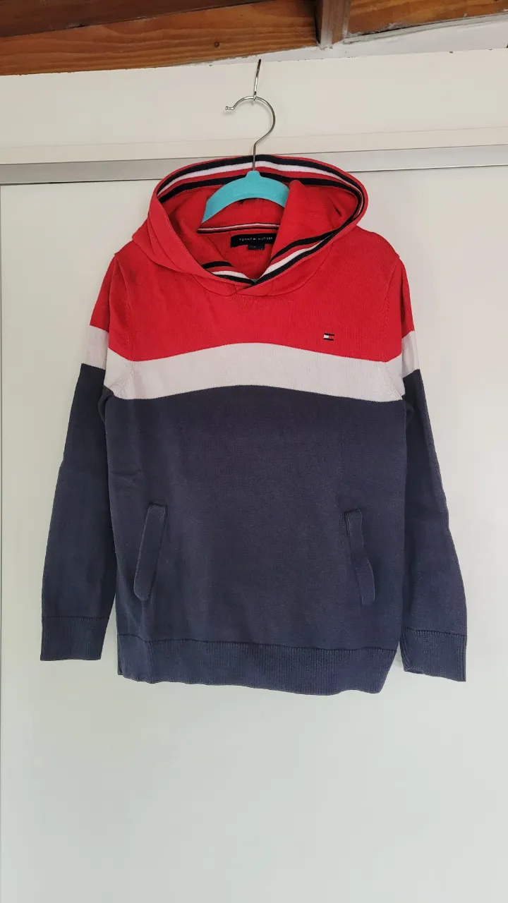 Buzo con capucha de algodón, de mangas largas, con estampa de líneas horizontales en rojo, blanco y azul marino. Posee bolsillo tipo canguro al frente.