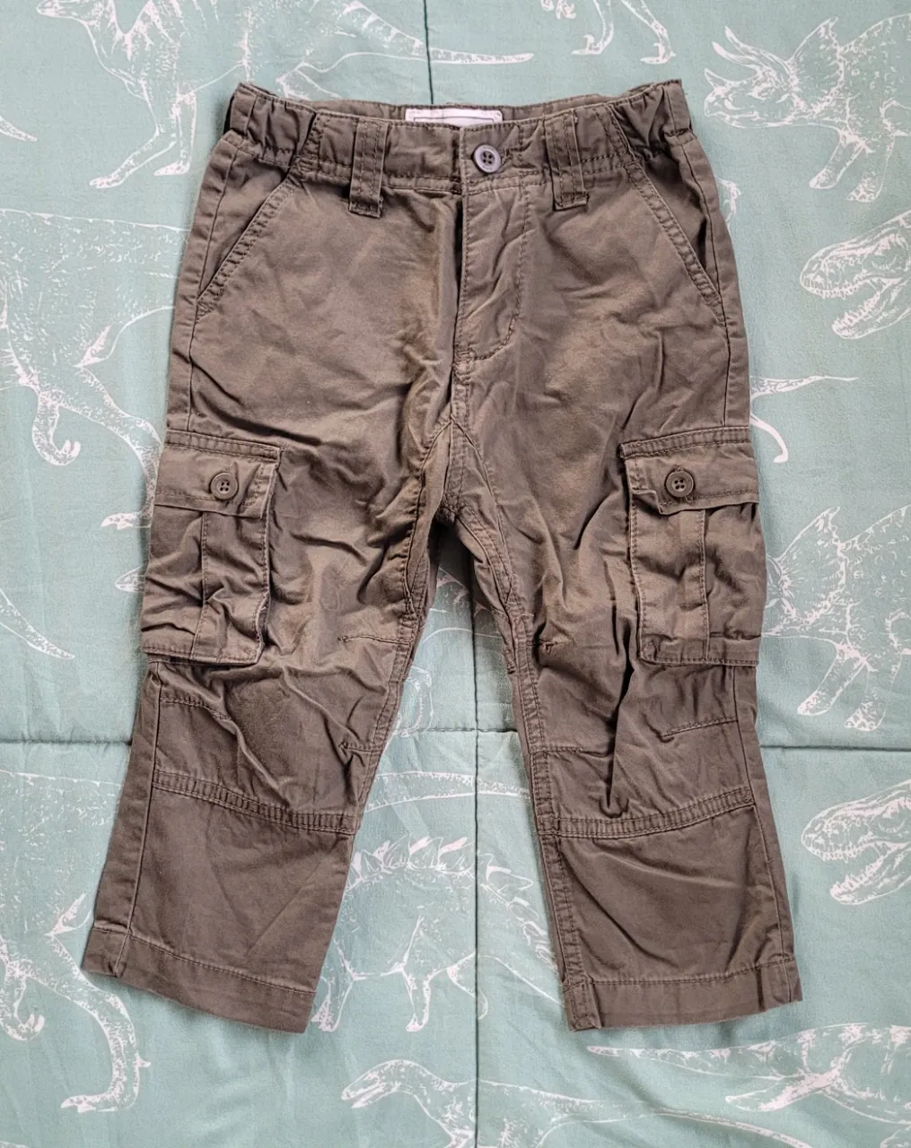 Pantalón cargo de color verde militar. Posee bolsillos con tapa y botón en los laterales y en la parte trasera. Cierre con botón y presilla.