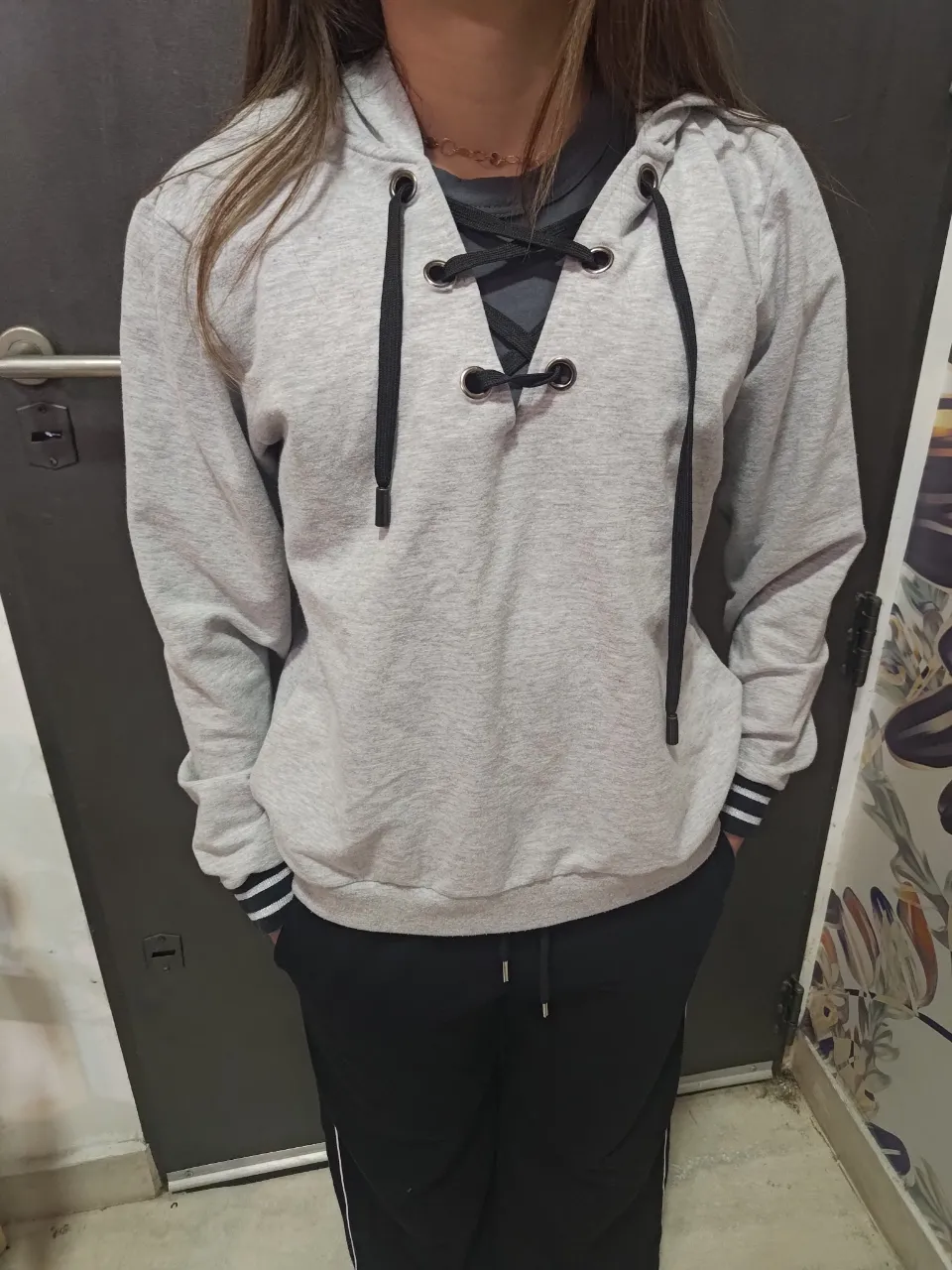 Hoodie gris claro con cordones negros y detalles de rayas en los puños. Ideal para un look casual y cómodo.