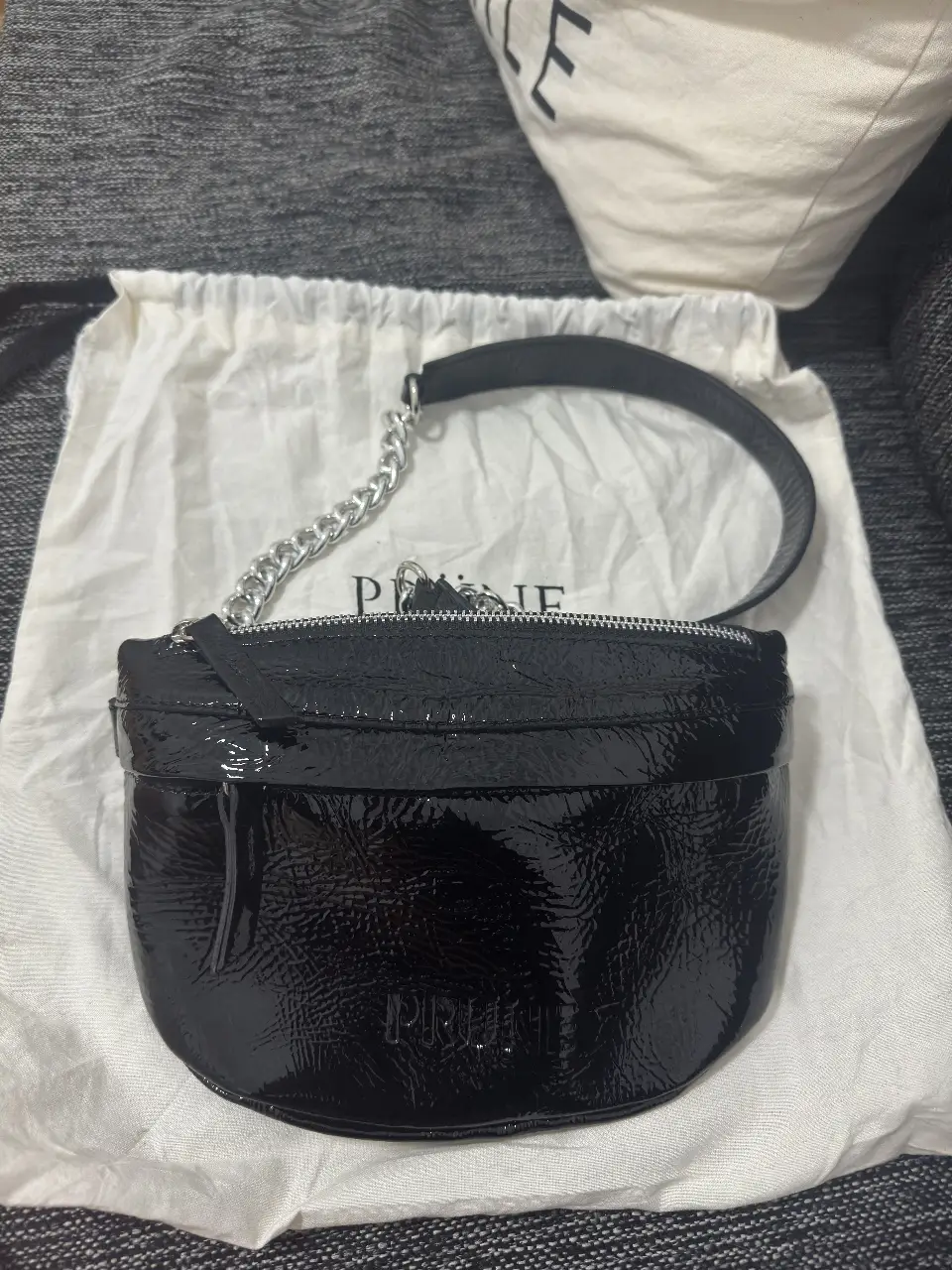 Cartera bandolera negra de charol, con cadena plateada y correa para el hombro. Ideal para llevar lo esencial con estilo y elegancia.