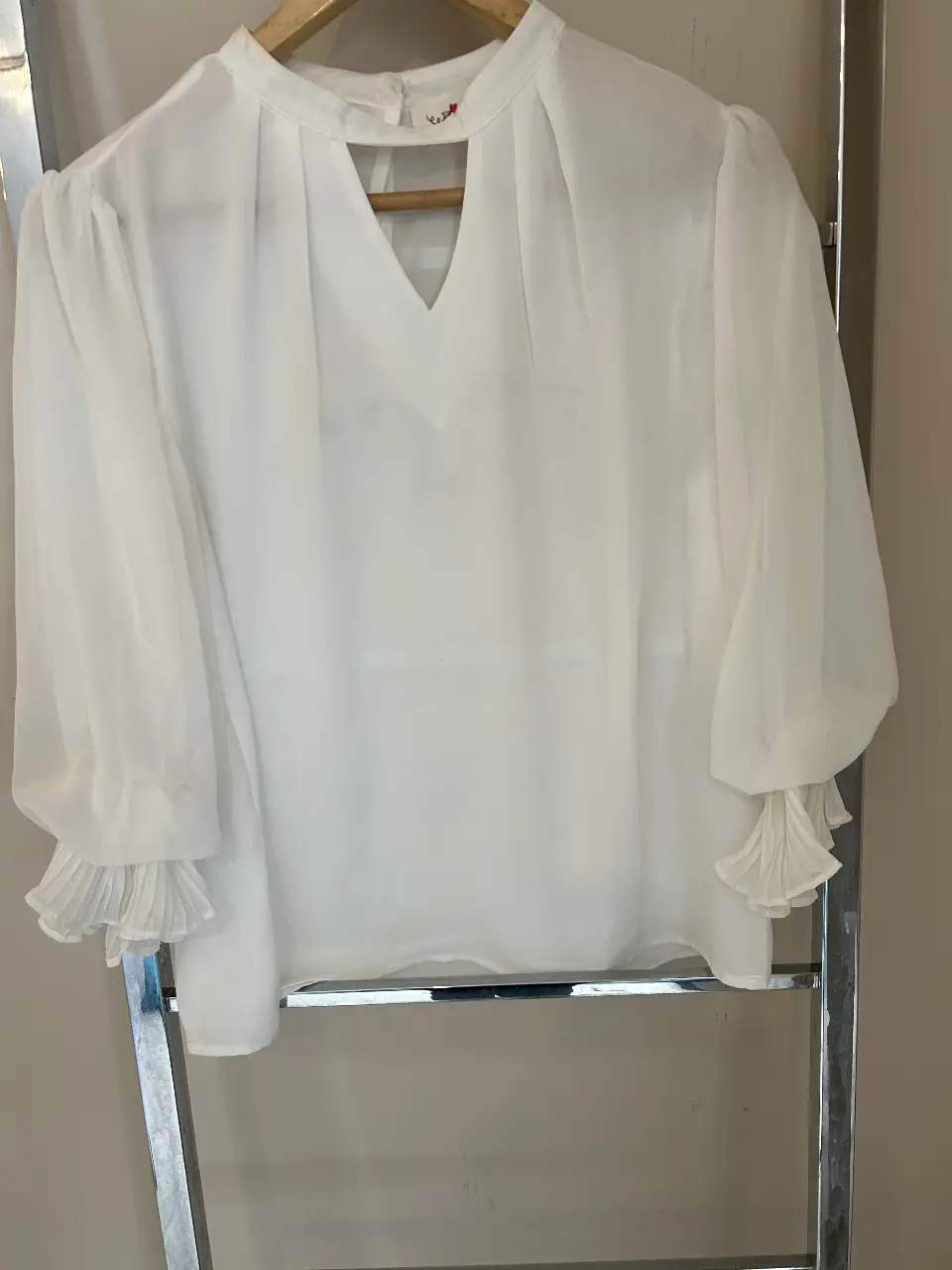 Blusa blanca con mangas largas abullonadas y detalles de volados en los puños. Cuello redondo con abertura en V. Ideal para un look elegante y sofisticado.