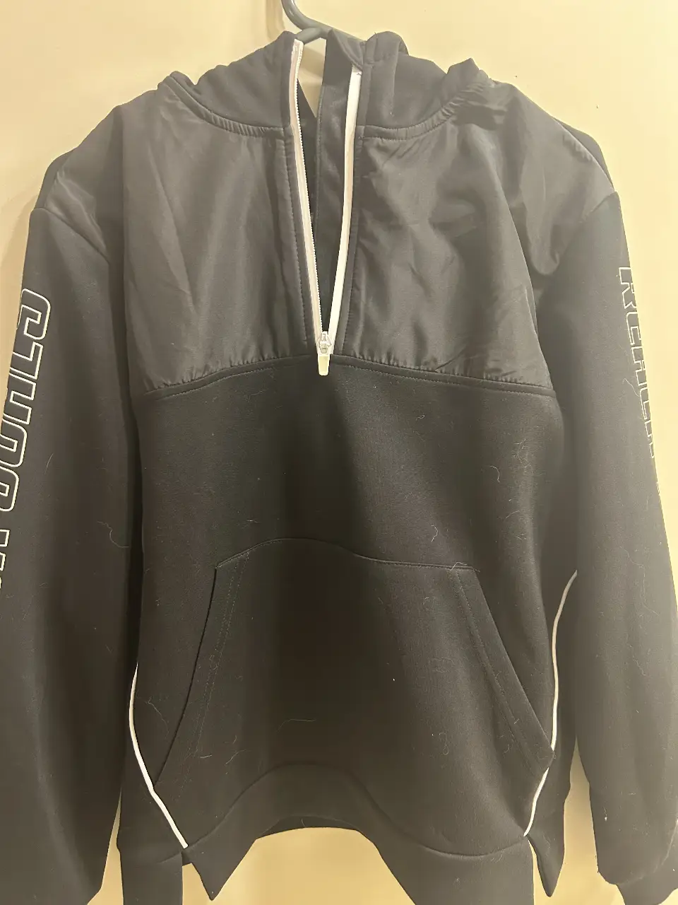 Buzo con cierre negro con detalles blancos y capucha. Tiene un bolsillo tipo canguro y la frase "REACH YOUR GOALS" en las mangas. Ideal para un look deportivo y casual.