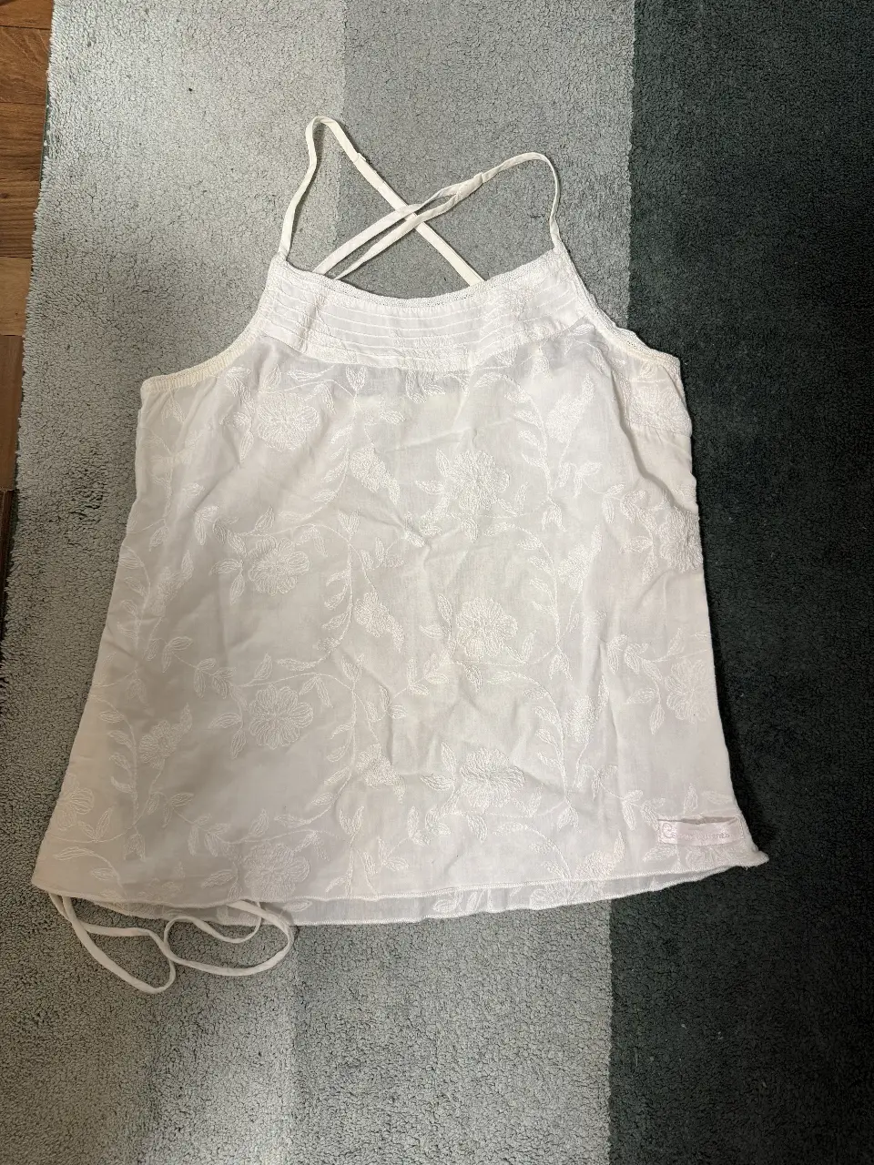 Top blanco con bordado floral, ideal para un look fresco y femenino. Con tirantes cruzados en la espalda y detalles de ajuste en los laterales. cierre lateral invisible y en el lado opuesto y abajo tiritas para frunzir