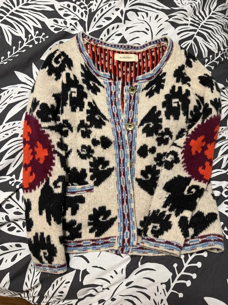 Cardigan tejido con diseño floral en tonos crudos y negros, con detalles en naranja y azul. Ideal para un look bohemio y abrigado. material lana de mohair, es bien grueso.
