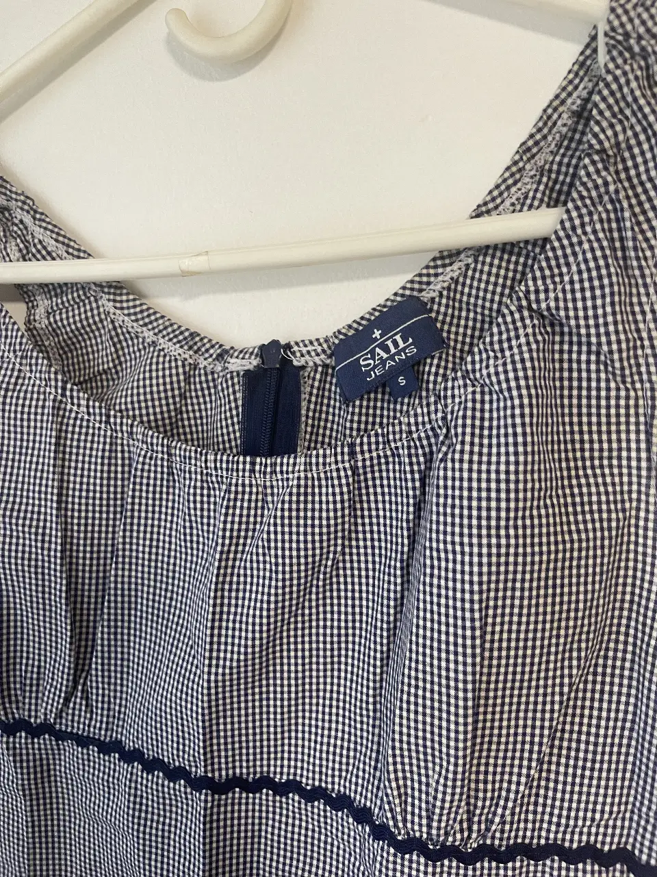 Vestido mini de mujer, con estampado de cuadros en blanco y azul. Tiene un cierre en la parte trasera y detalles en azul marino en el borde inferior y en la cintura. Ideal para un look casual y fresco y veraniego
