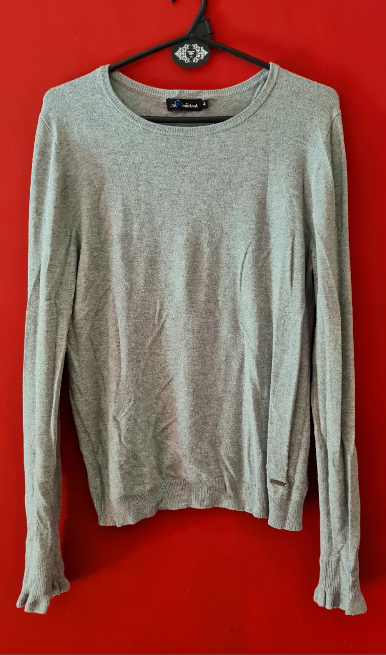 Sweater gris de manga larga con cuello redondo y detalles acampanados en los puños. Un básico súper cómodo y versátil para tu día a día.