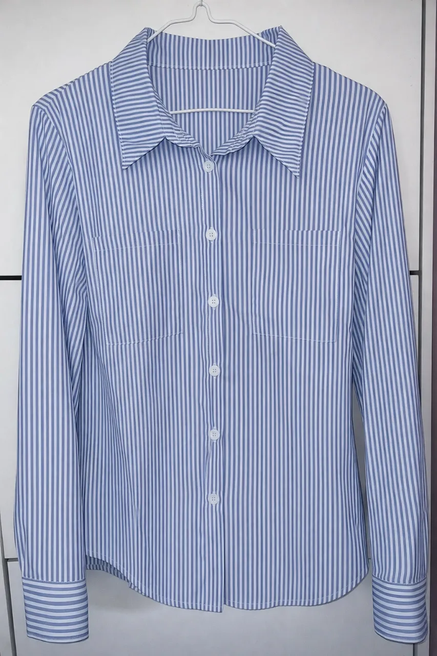Camisa de vestir a rayas celestes y blancas, con cuello clásico y botones al frente. Posee puños abotonados. Ideal para un look formal o casual.