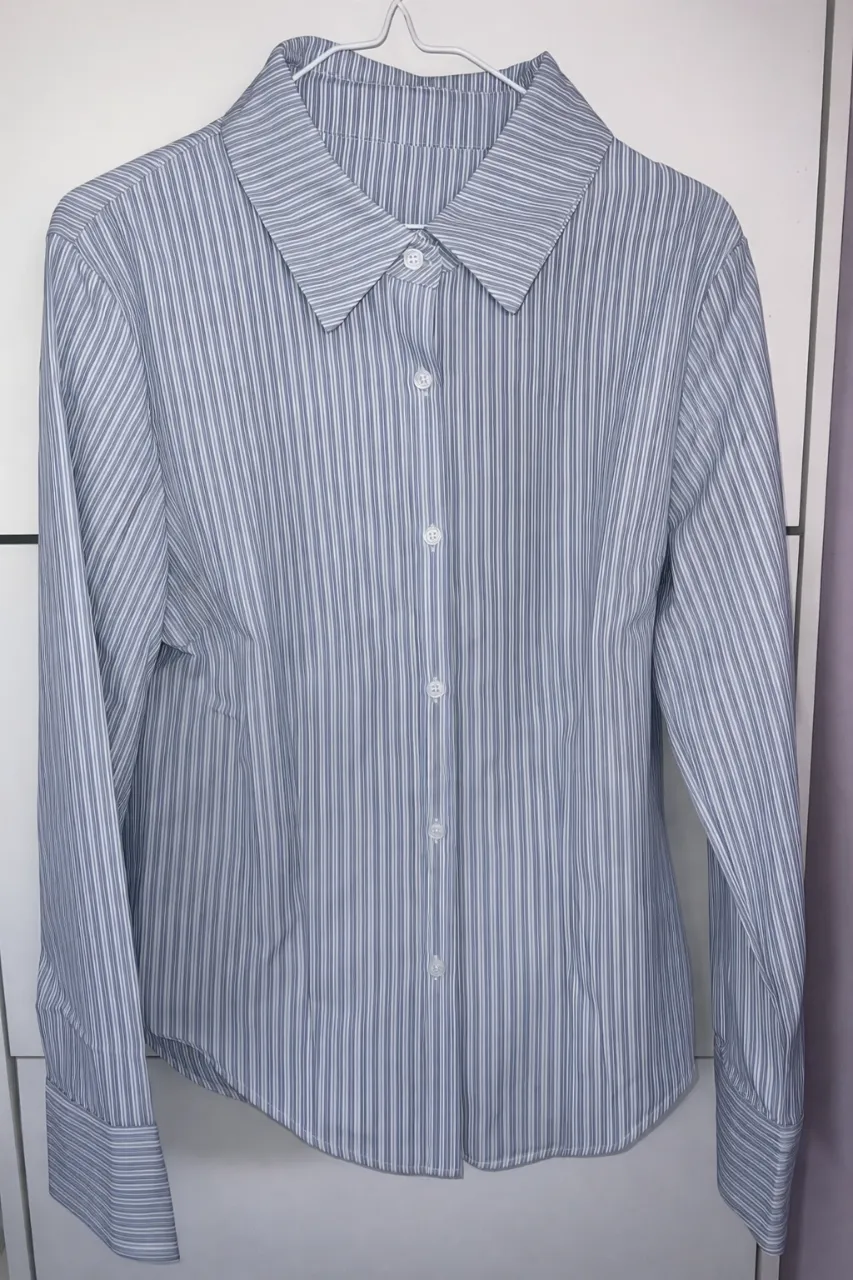 Camisa a rayas manga larga, ideal para un look casual o de trabajo. Su diseño clásico la hace versátil y fácil de combinar.