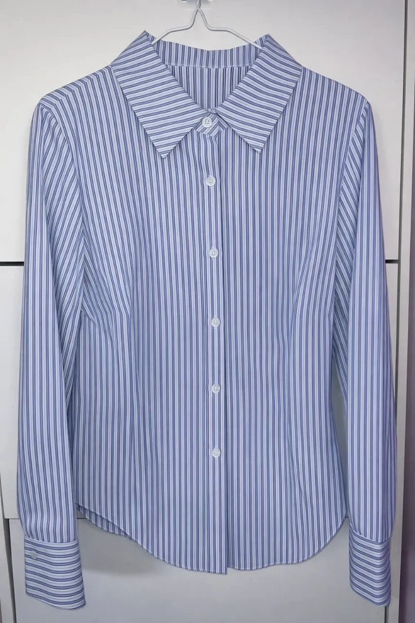 Camisa de vestir a rayas verticales en tonos de azul y blanco. Posee cuello clásico, botones al frente y puños con botones. Ideal para un look formal o de trabajo.