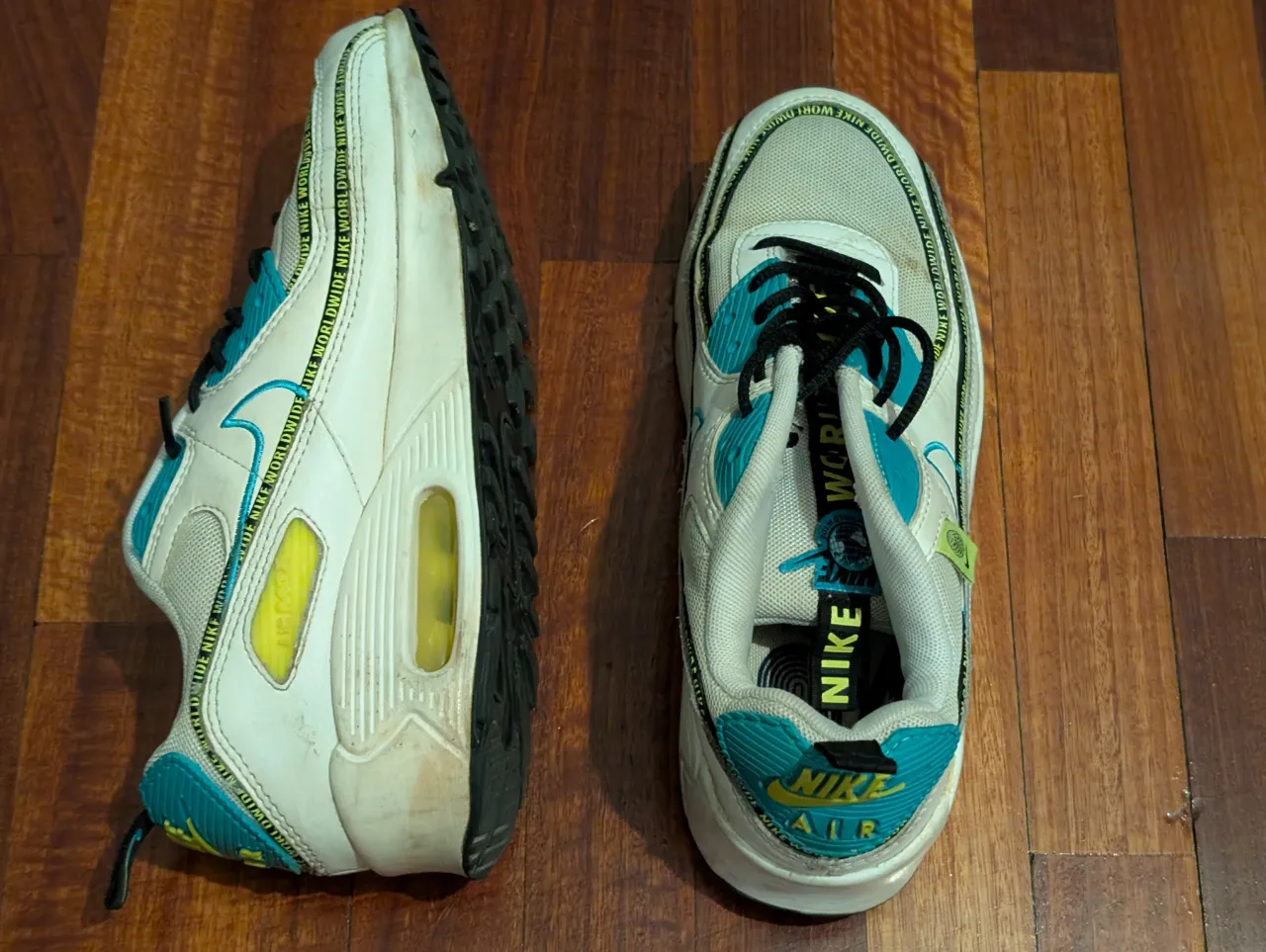 Zapatillas Nike Air Max 90 World, blancas con detalles en azul y amarillo. Diseño icónico y cómodo para uso diario.