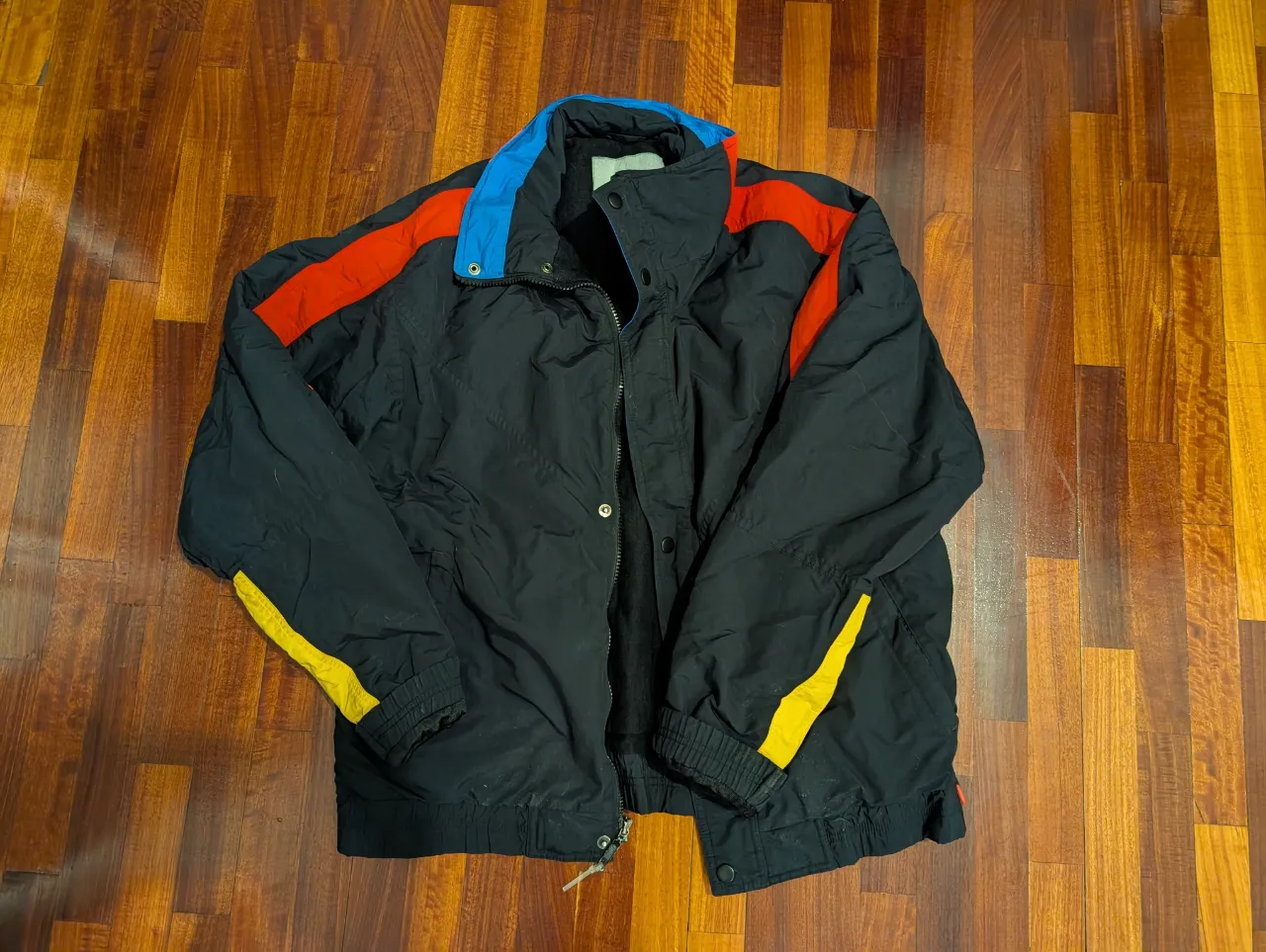 Campera deportiva negra con detalles en rojo y amarillo. Ideal para actividades al aire libre o uso casual. Diseño retro.