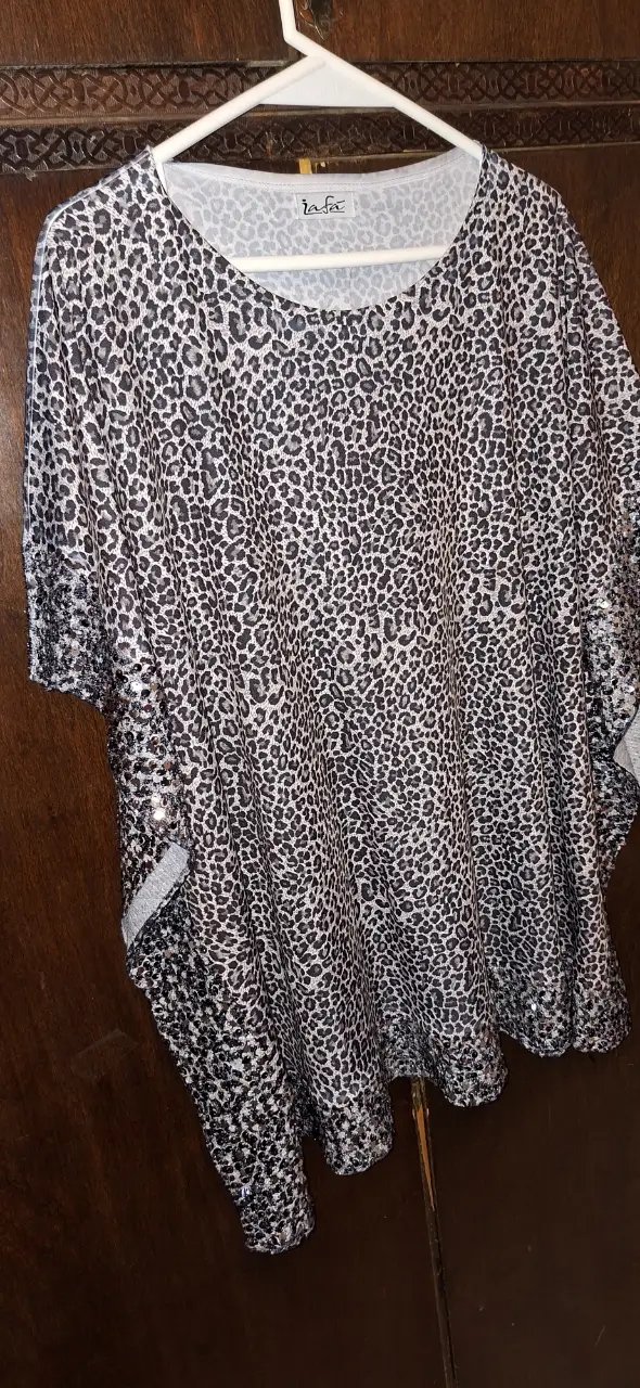Blusa de mujer con estampado de leopardo en tonos grises y blancos. Diseño holgado con mangas cortas y detalles de lentejuelas en los bordes. Ideal para un look casual y moderno.