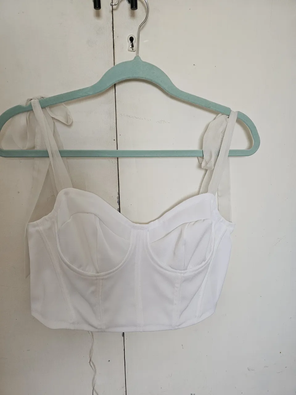 Top corset blanco con breteles de lazo. Ideal para un look elegante y moderno. Perfecto para combinar con faldas o pantalones de cintura alta.
