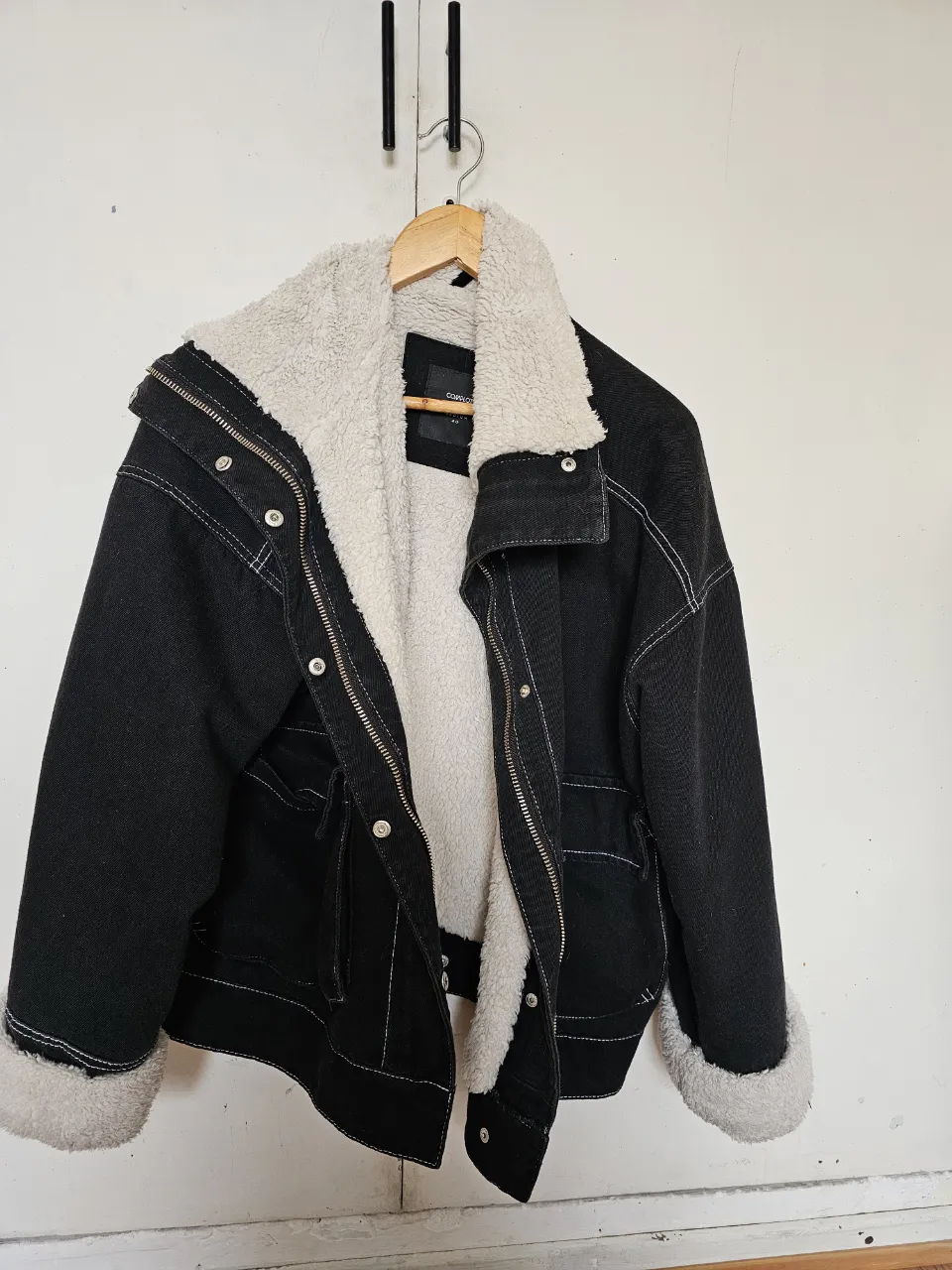 Campera de jean negra con interior y cuello de piel sintética color crema. Detalles de costuras blancas y bolsillos. Oversize. Ideal para un look casual y abrigado. Se le salieron 3 brochecitos, a volver a colocar.
