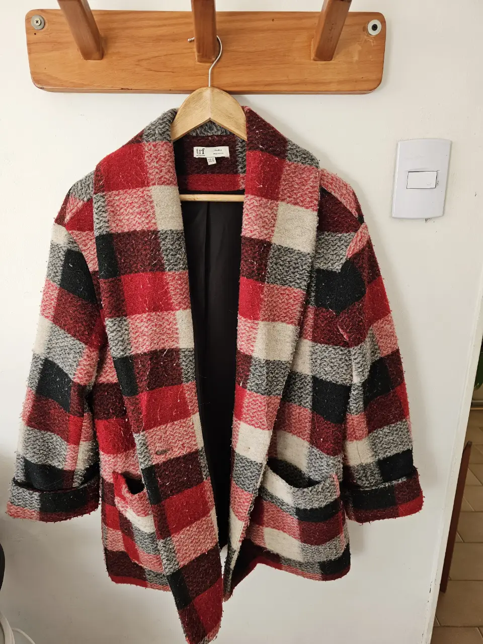 Tapado amplio de paño a cuadros en tonos rojos, grises y negros. Corte clásico con solapas y bolsillos. Ideal para un look de invierno con estilo.