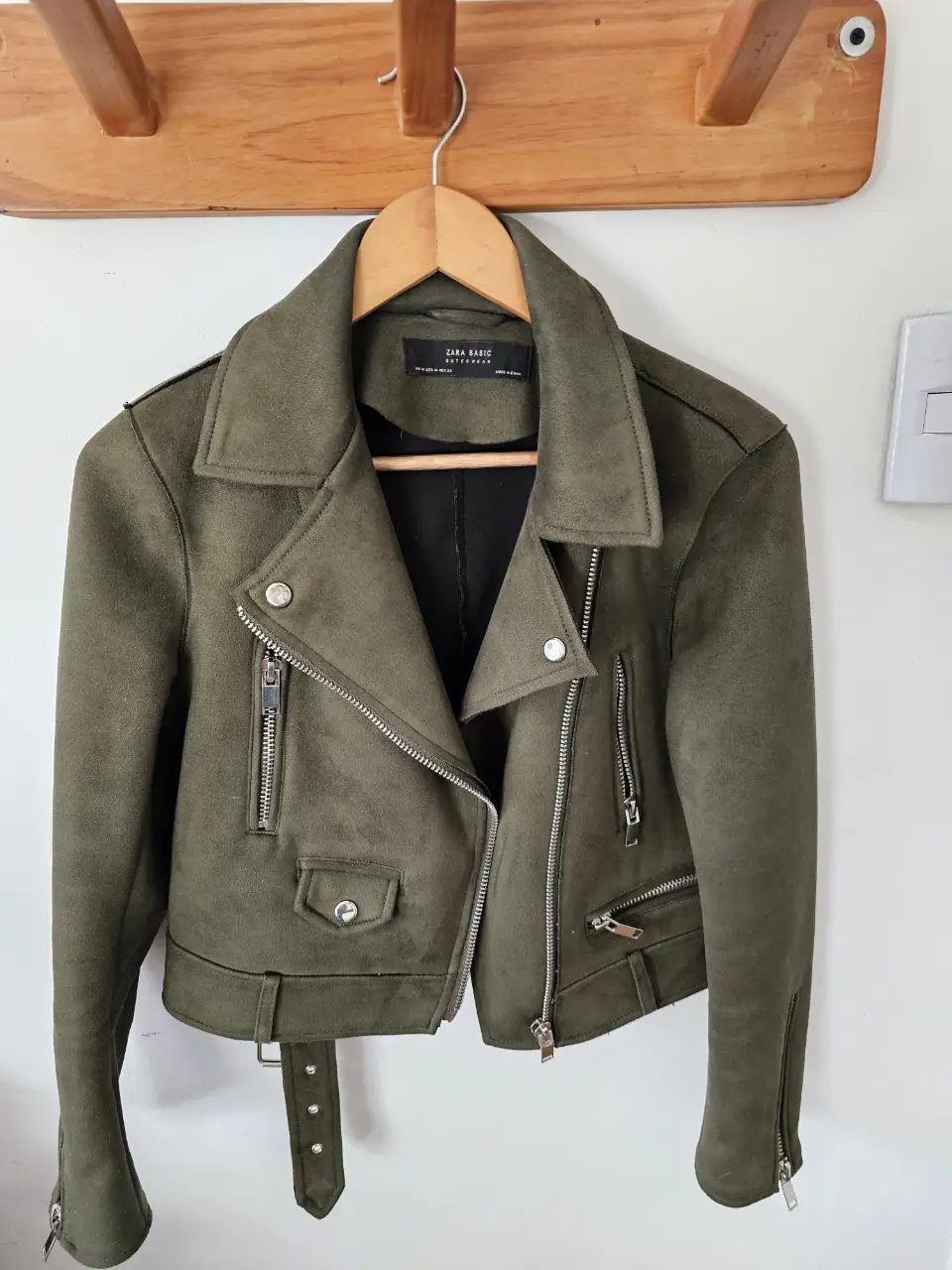 Campera biker de gamuza sintética verde oscuro, con cierre asimétrico y detalles metálicos. Ideal para un look moderno y canchero. Incluye cinturón.