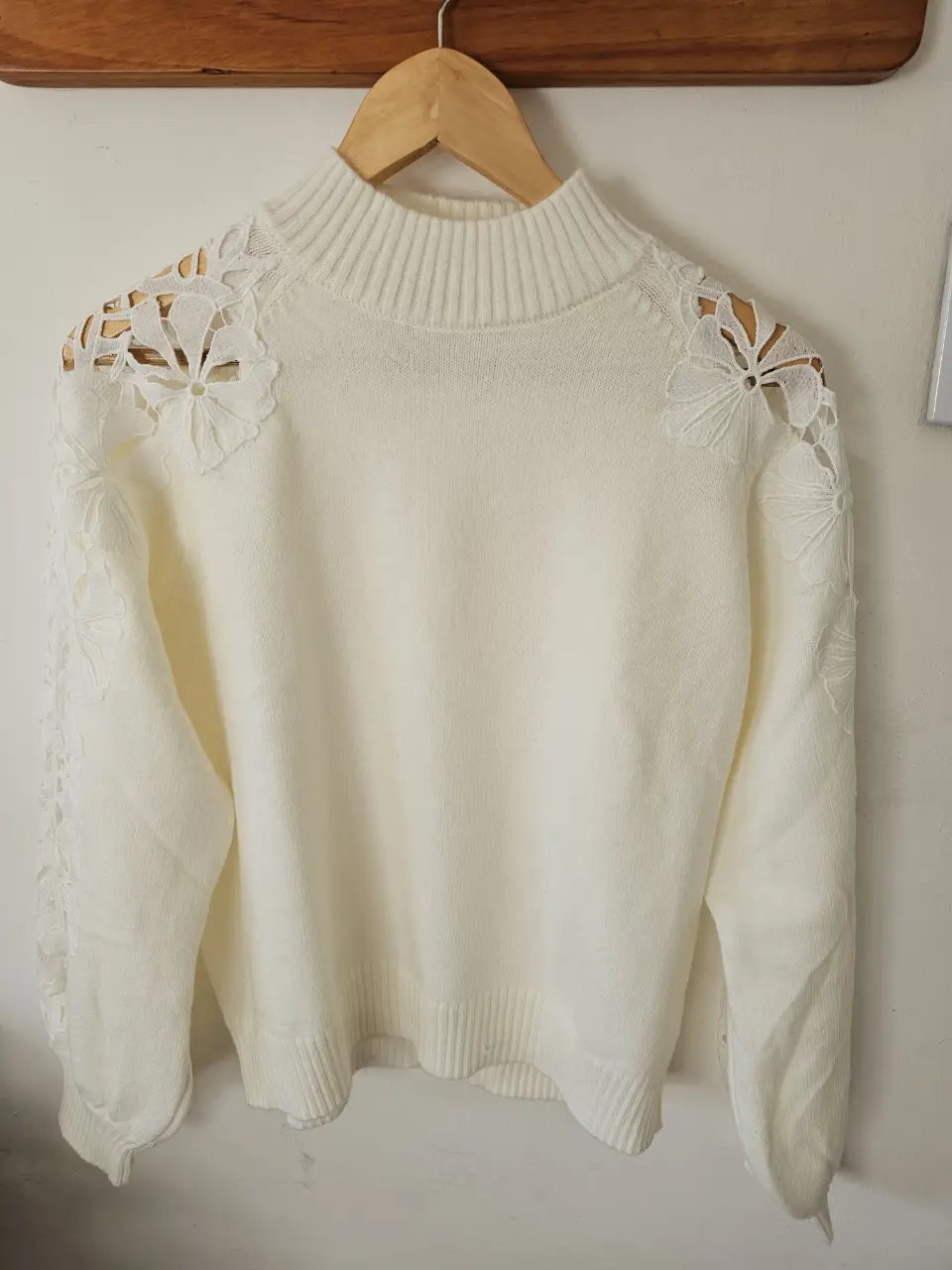 Sweater de cuello alto color blanco con detalles florales en los hombros. Ideal para un look elegante y abrigado.