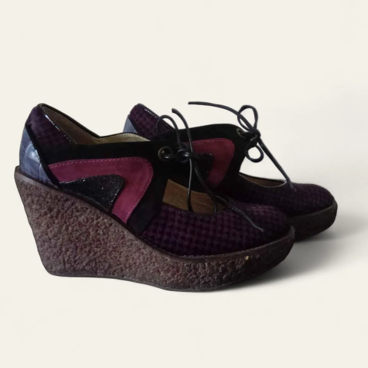 Zapatos de plataforma con taco cuña, estilo Mary Jane, en color violeta oscuro y detalles en fucsia y negro. Tienen cordones finos para atar.