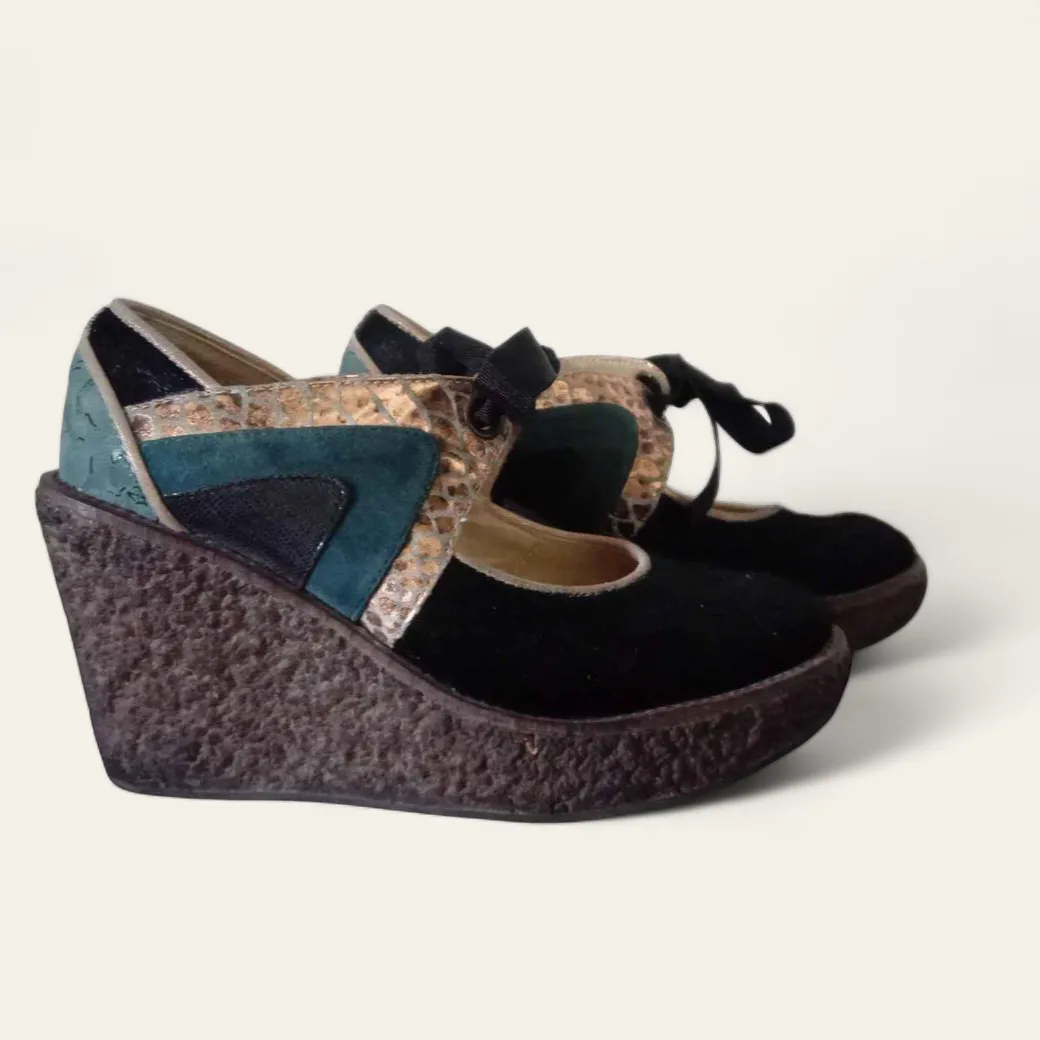 ¡Zuecos súper originales y cancheros! Tienen una plataforma alta tipo cuña con textura, y la capellada combina gamuza negra, detalles en dorado con textura de serpiente y parches en verde turquesa y negro. Tienen una tira con moño negro que cruza el empeine. ¡Ideales para darle un toque único a cualquier look!