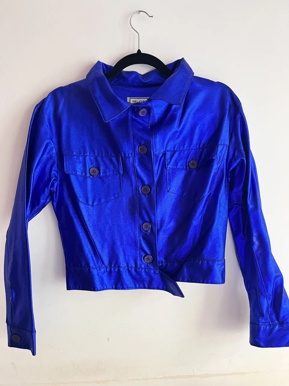 Campera azul brillante con botones al frente y dos bolsillos en el pecho. Cuello camisero.