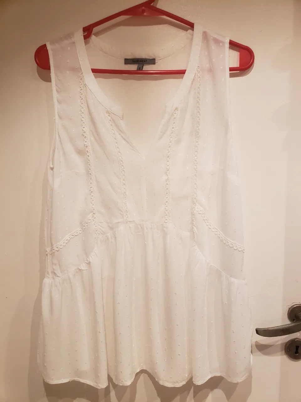 Blusa blanca sin mangas, con detalles de puntillas y bordados sutiles. Posee un corte holgado y con volado en la parte inferior, ideal para un look fresco y femenino.