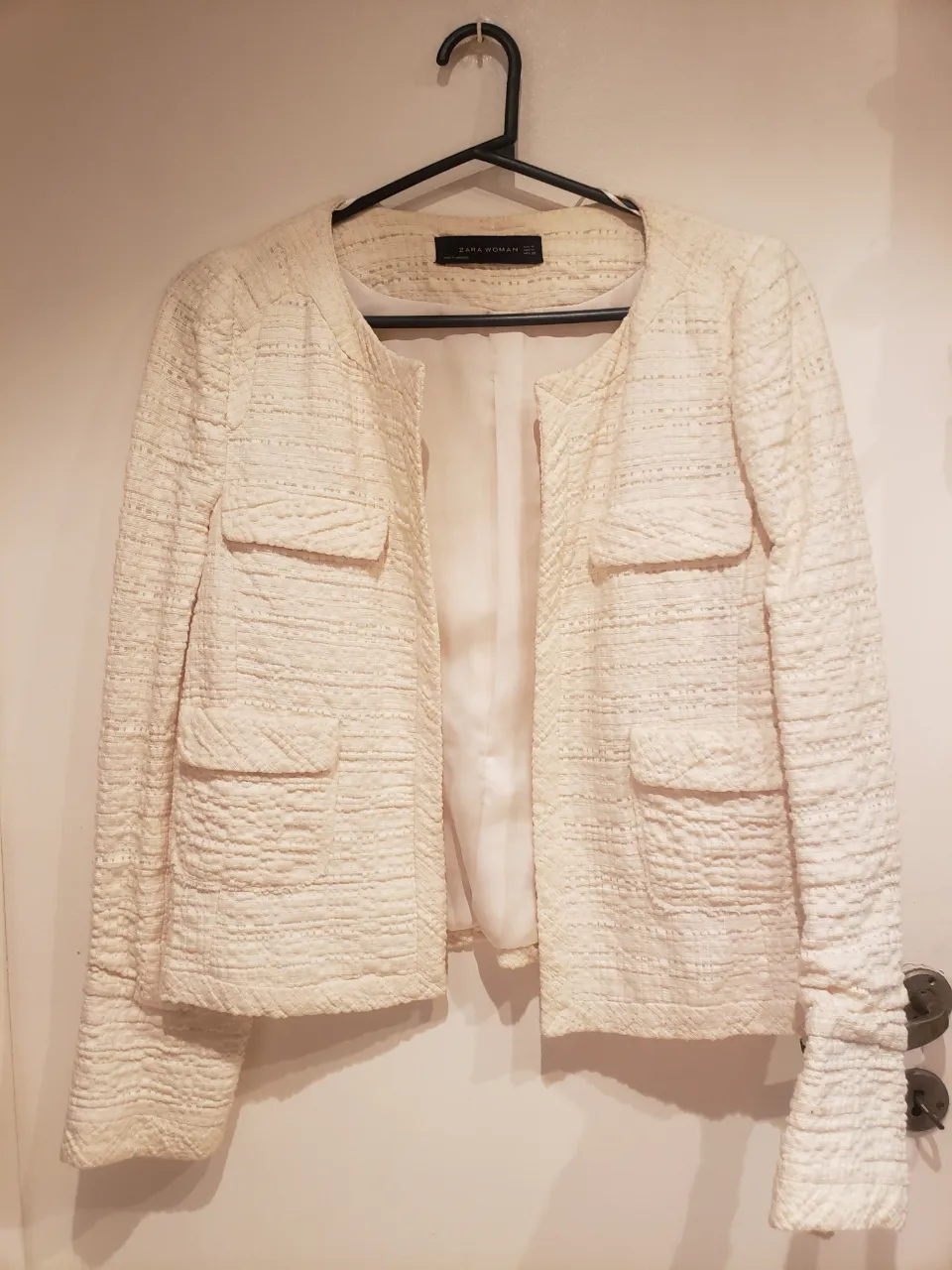 Chaqueta de tweed color crudo, con botones plateados en los puños y bolsillos. Ideal para un look elegante y sofisticado.