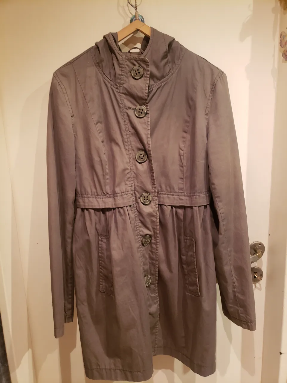 Campera impermeable de color gris oscuro, ideal para días de lluvia o entretiempo. Posee capucha, cierre de botones y bolsillos frontales. Su diseño es moderno y funcional, perfecta para un look casual y cómodo.