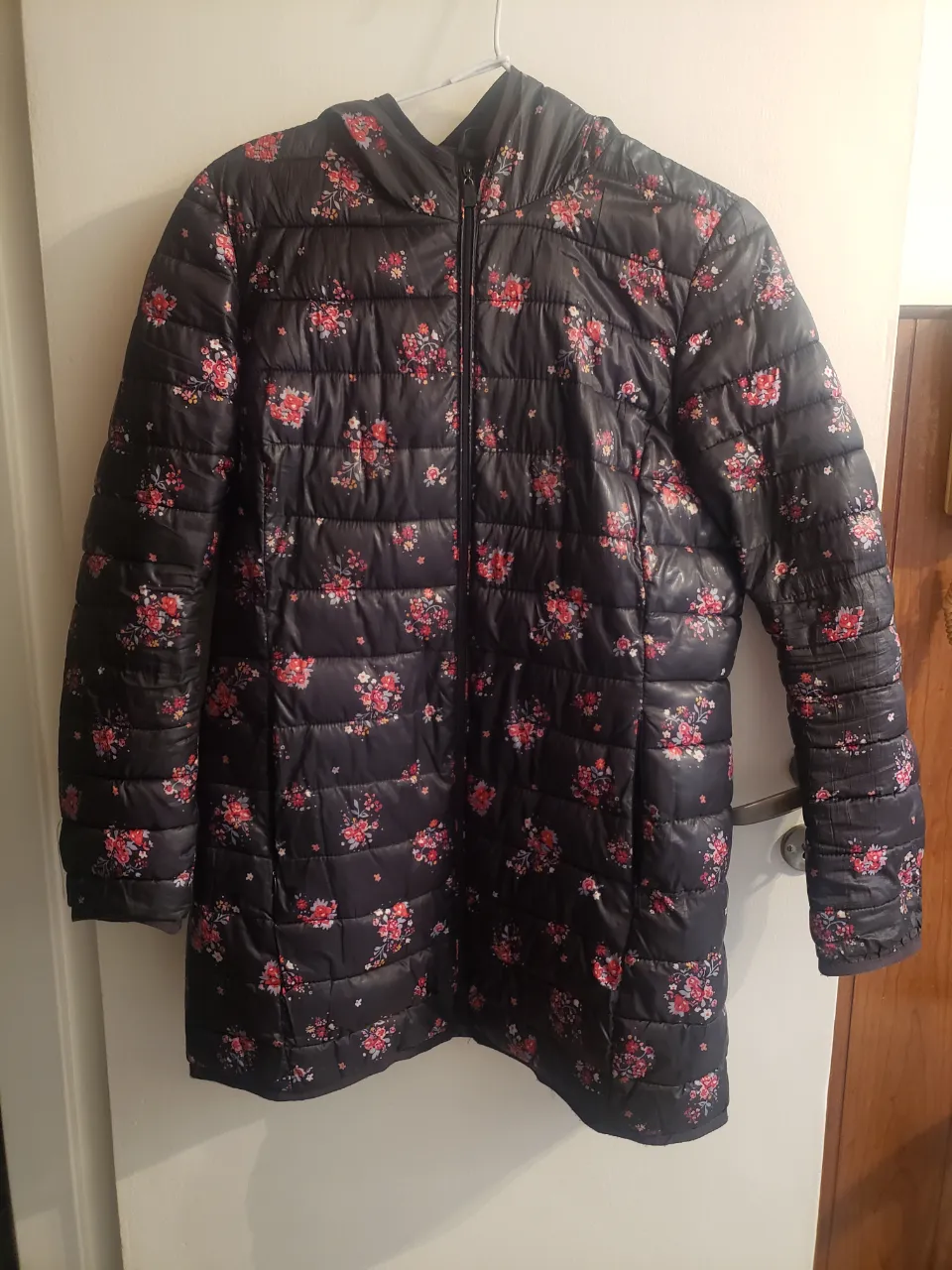 Campera acolchada negra con estampado floral de flores rojas y rosas. Tiene capucha y cierre al frente. Ideal para un look casual y abrigado.