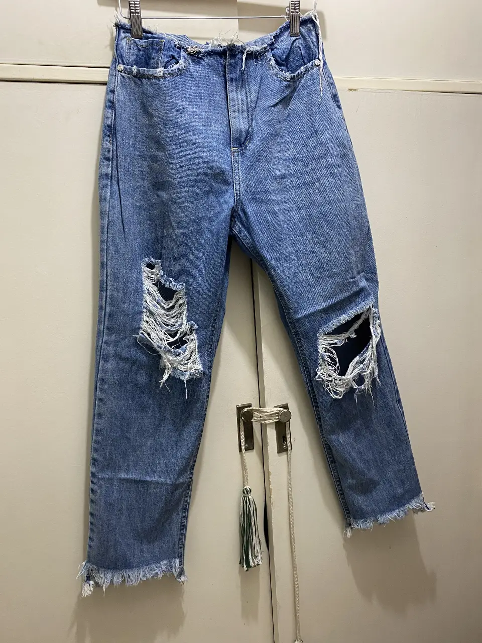 Jeans de mujer, tiro medio, con roturas en las rodillas y flecos en el bajo. Corte recto, ideal para un look casual y moderno.