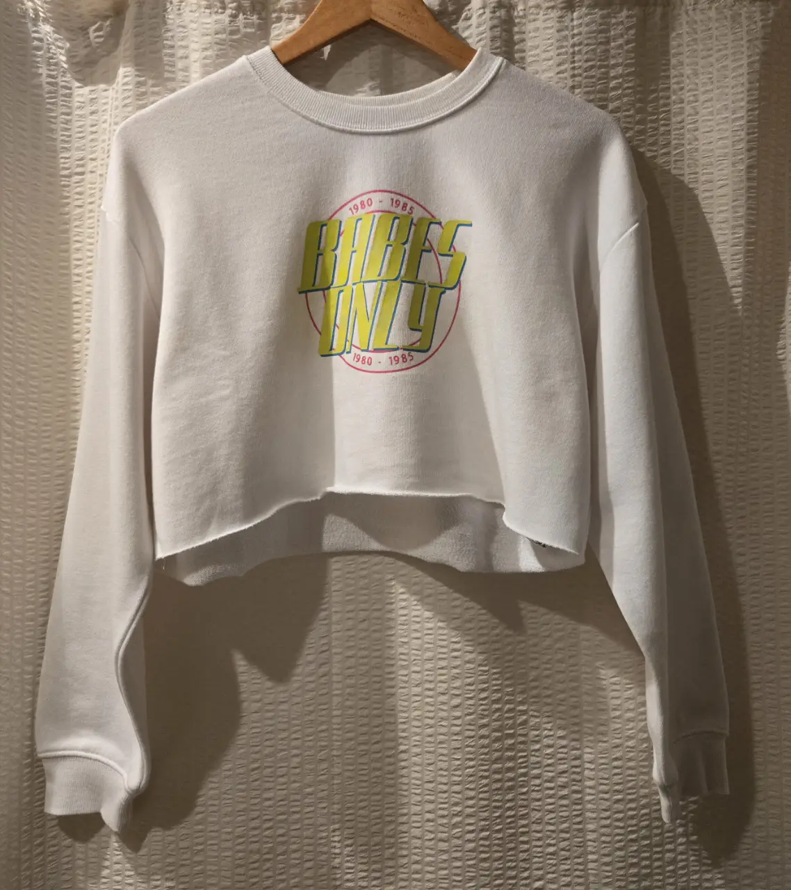 Buzo crop blanco con estampado "Babes Only" en amarillo y rosa. 60% algodon 40% poliester
