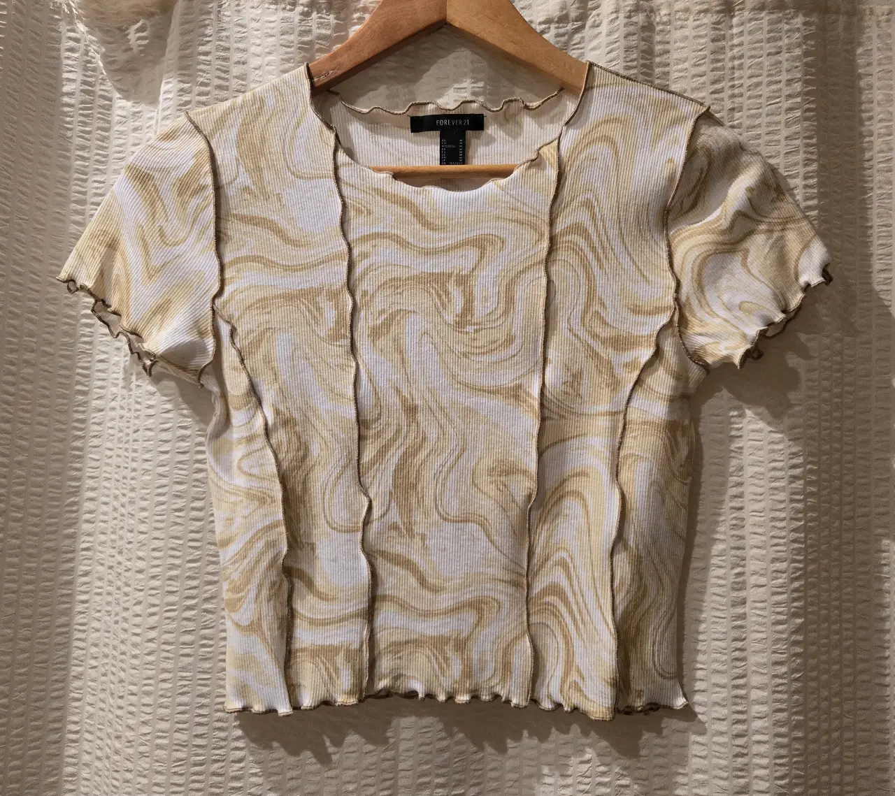 Remera manga corta con estampado de diseño tipo mármol en tonos amarillos y blancos. Corte ajustado con detalles de costuras a la vista y bordes ondulados costura rulotte. Talle M equivale a S. 58% algodón 37% poliester 5% spandex