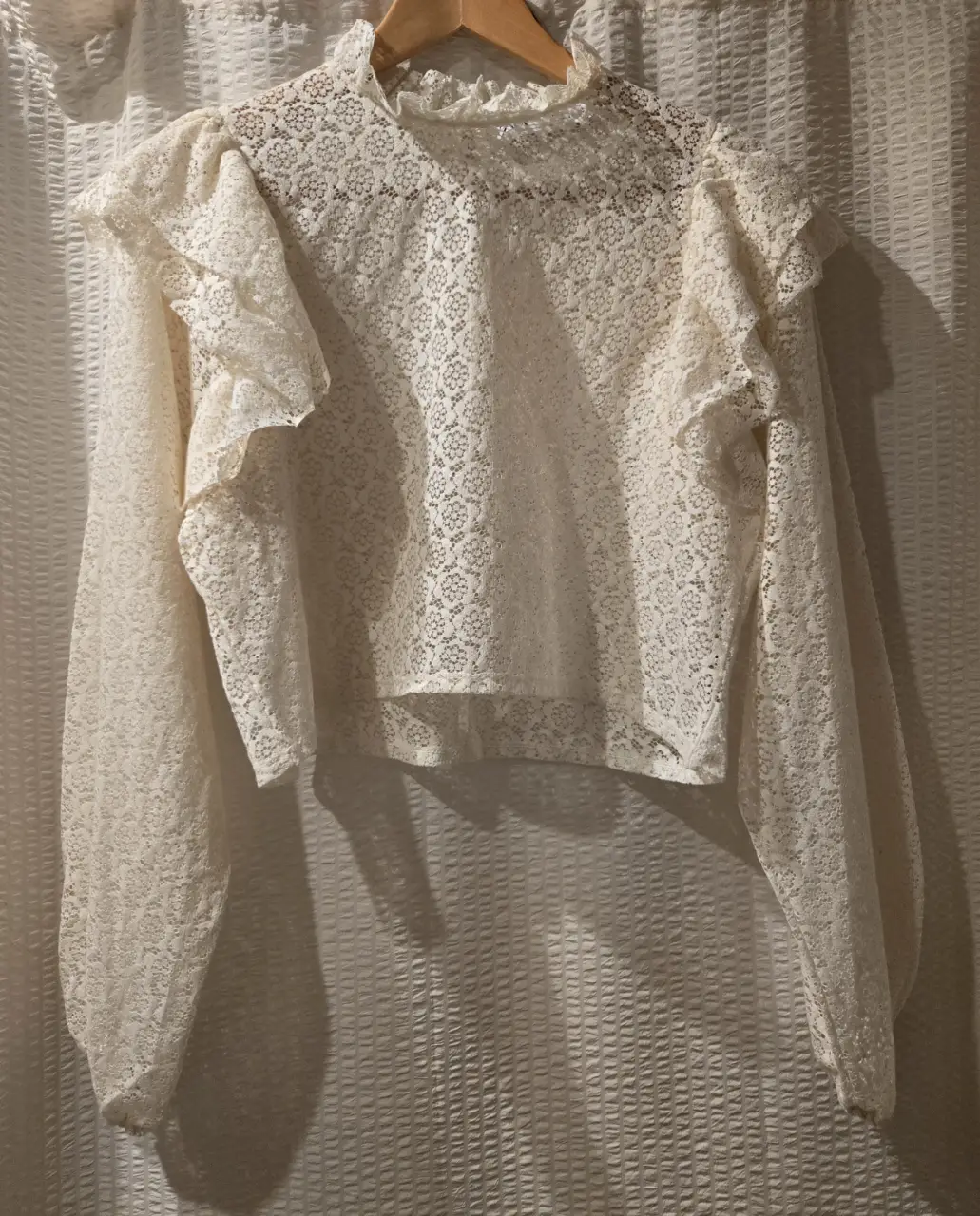 Blusa de encaje color crudo de la marca Zara, con mangas largas abullonadas y volados en los hombros y en el cuello. 52% algodon 39% poliamida 9% elastano