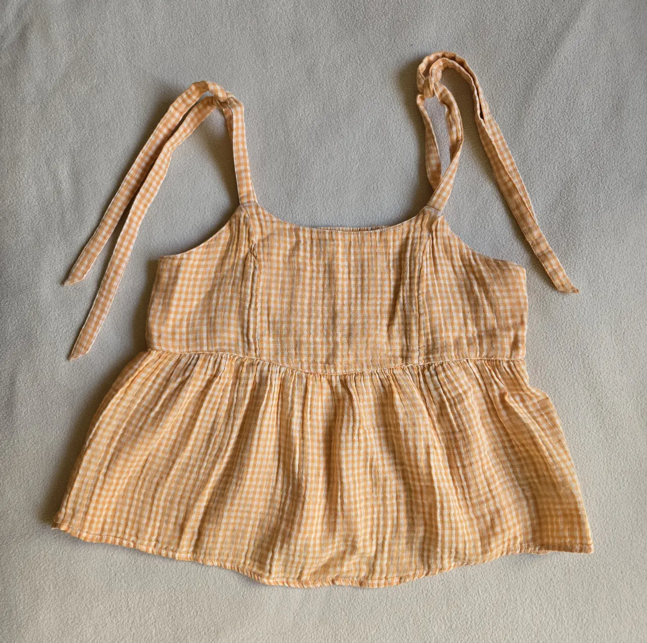 Top de mujer con diseño vichy en color naranja y blanco. Confeccionado en tela liviana y fresca, ideal para el verano. Cuenta con tirantes ajustables y un corte holgado que favorece la comodidad