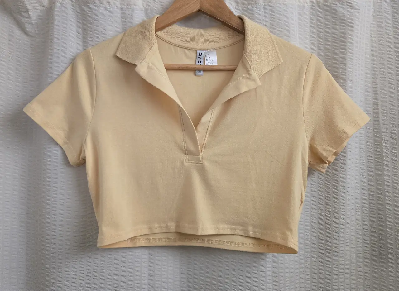 Remera crop de mujer, color amarillo claro, con cuello polo y manga corta. 95% algodón 5% elastano