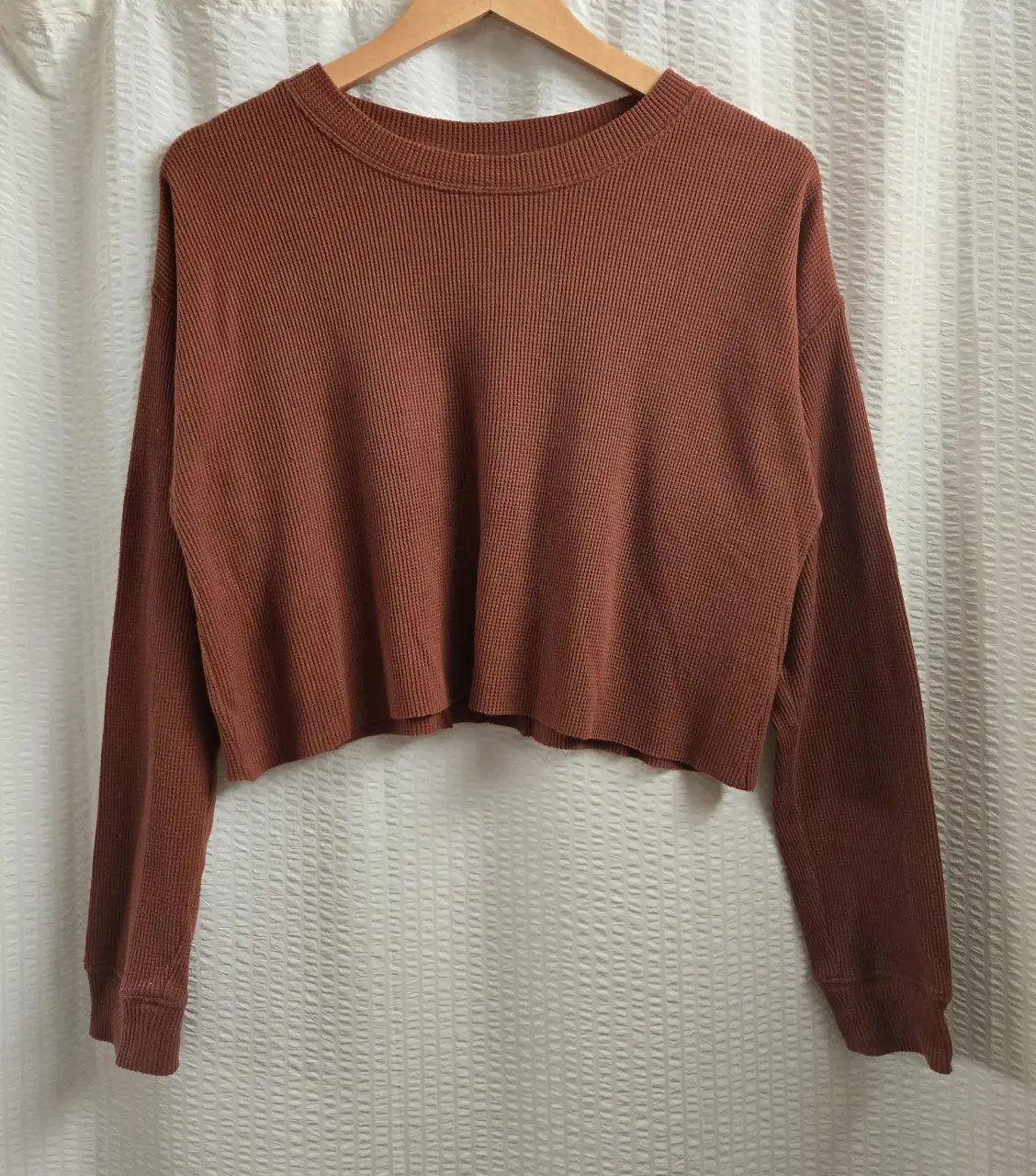 Remera crop de tejido waffle en color marrón ladrillo. Cuello redondo y mangas largas con puños. 60% algodón 40% poliester