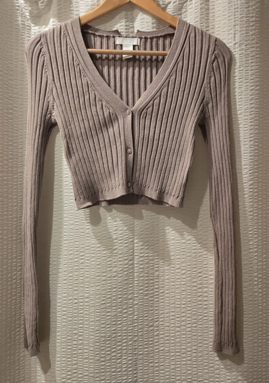 Cardigan tejido de punto acanalado en color visón. Escote en V y cartera con 3 botones. Ideal para un look casual y moderno. Tiene un tajo en el cuello en la parte de atrás, que se puede arreglar