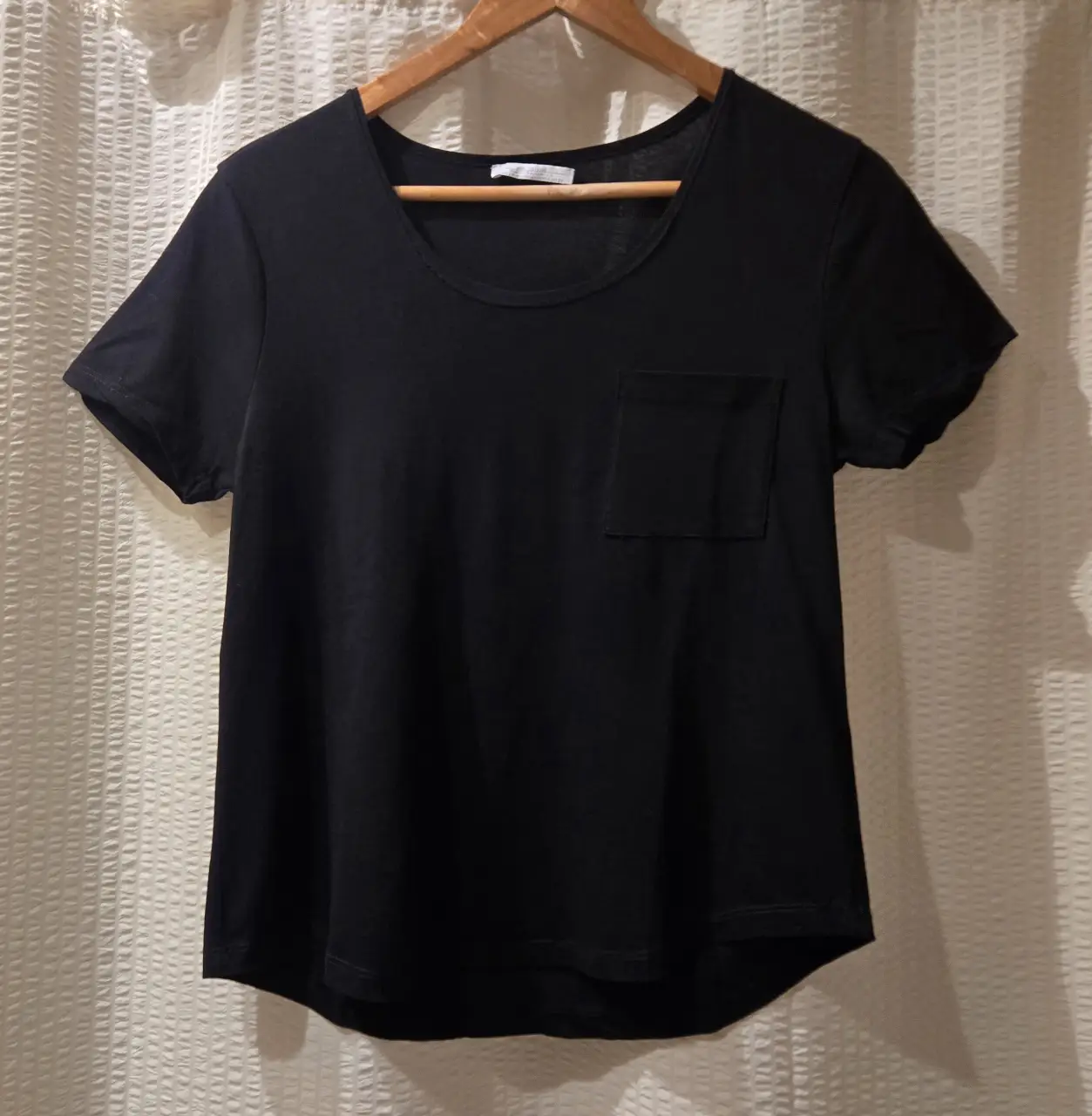 Remera negra de jersey de algodón, con cuello redondo y bolsillo en el pecho. Terminación redondeada