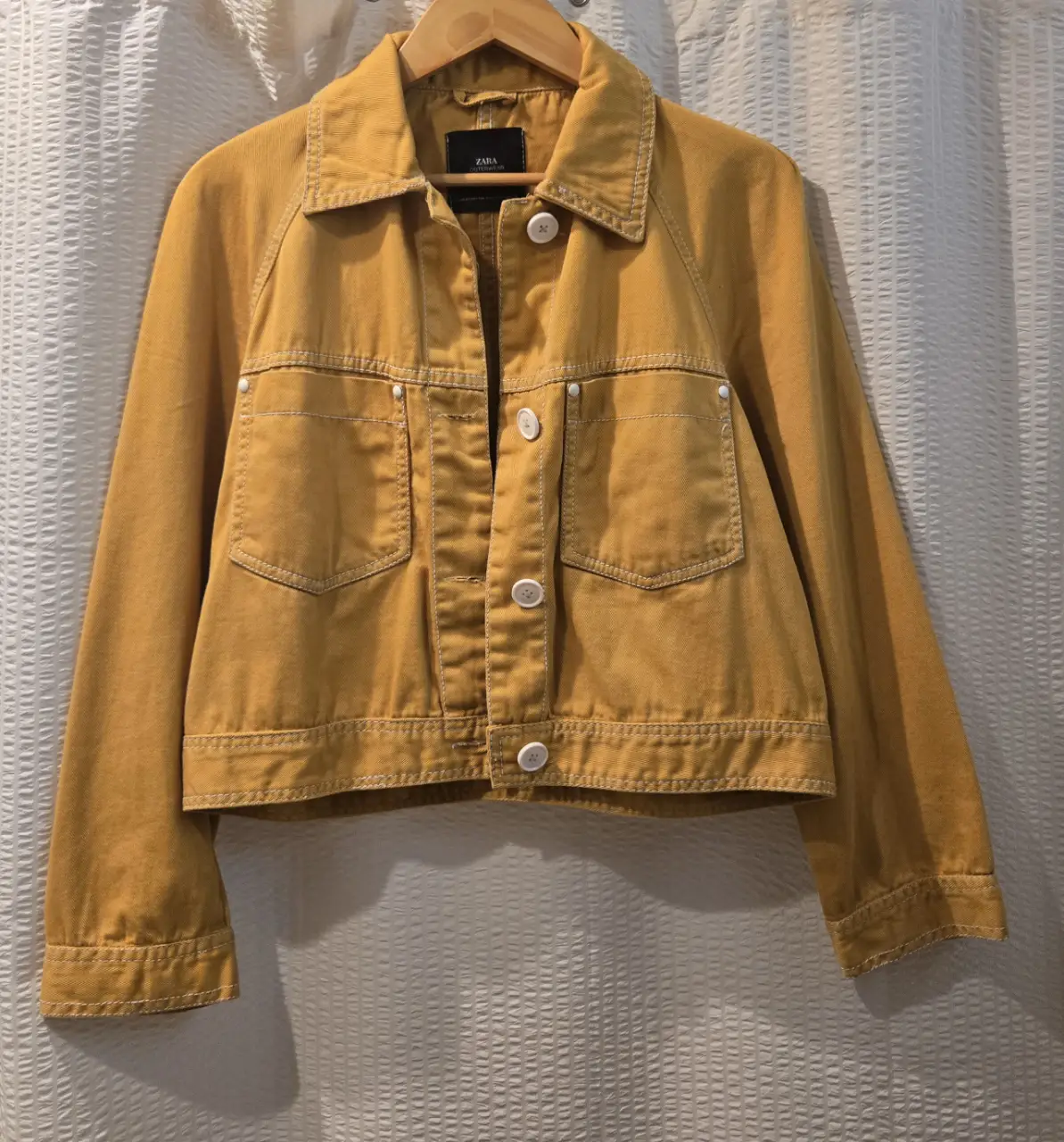 Campera de gabardina de Zara, color mostaza, con botones blancos y bolsillos delanteros. Ideal para un look casual y moderno. Corta y ancha. 100% algodón