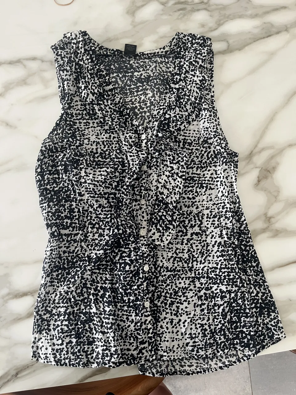 Blusa sin mangas con estampa animal print en blanco y negro. Posee botones al frente y un detalle de volados en la parte superior. Ideal para un look casual o de salida.