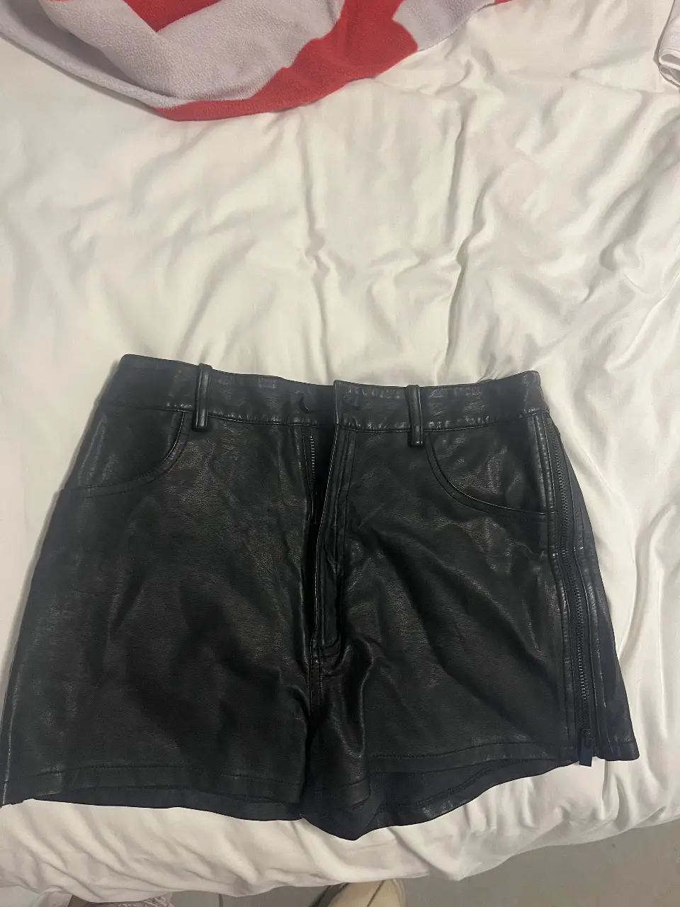 Short de cuero sintético negro, tiro alto, con cierre lateral y bolsillos delanteros. Ideal para un look moderno y audaz.