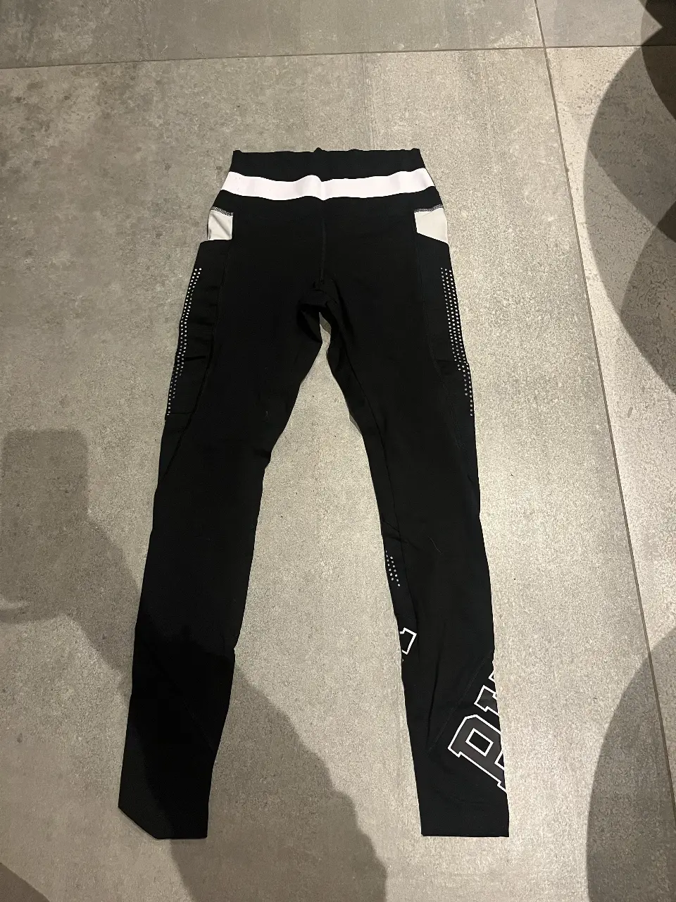 Calzas deportivas negras de la marca PINK, con detalles en blanco y bolsillos laterales. Ideales para entrenar.