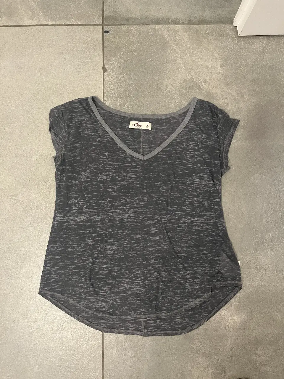 Remera de mujer Hollister, de manga corta y cuello en V. Confeccionada en un tejido jaspeado en tonos grises, ideal para un look casual y cómodo.
